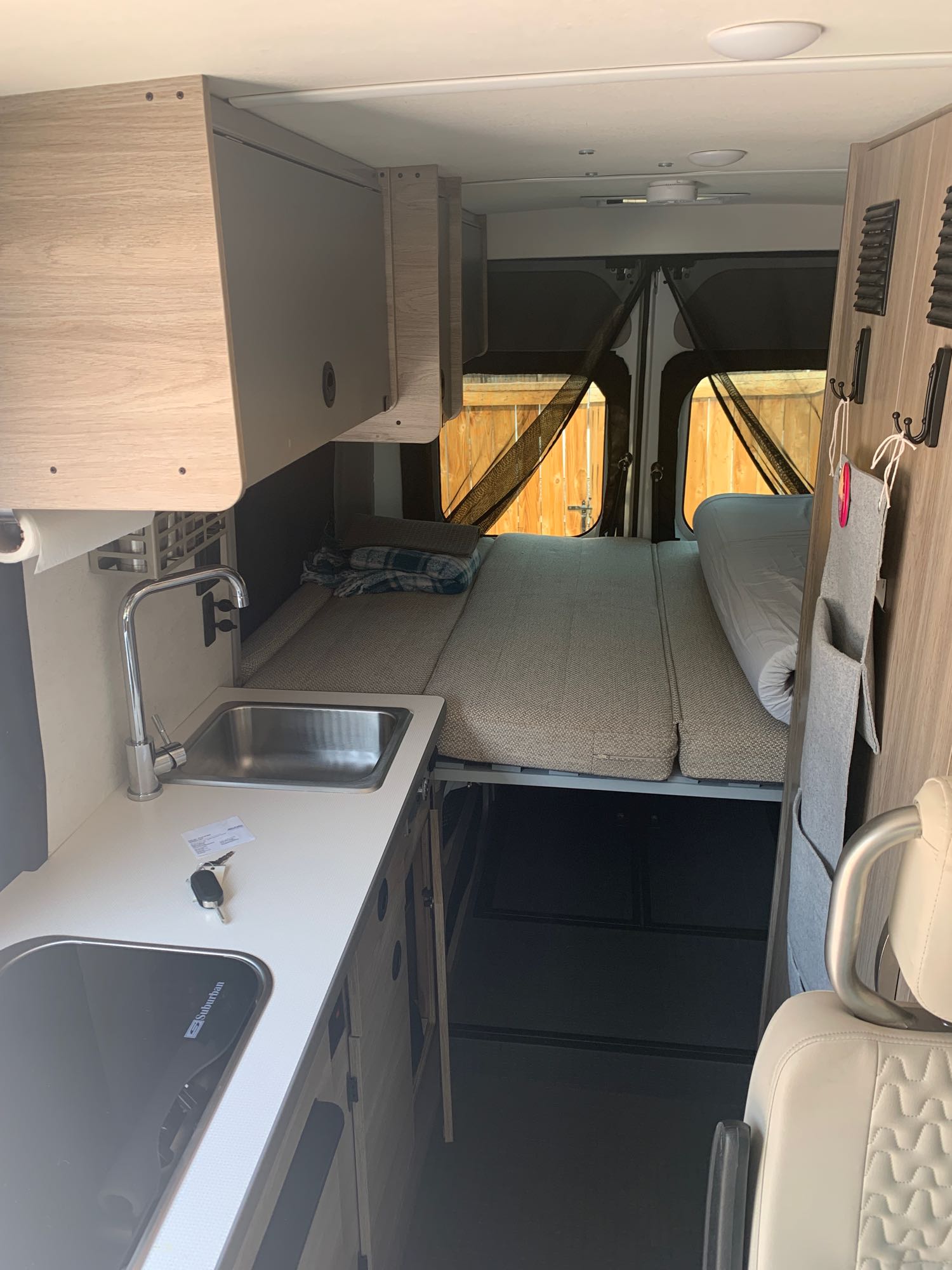 Inside an RV rental: a compact camper van interior featuring a bed, kitchen sink, stovetop, and overhead storage.. Winnebago Winnebago 2021