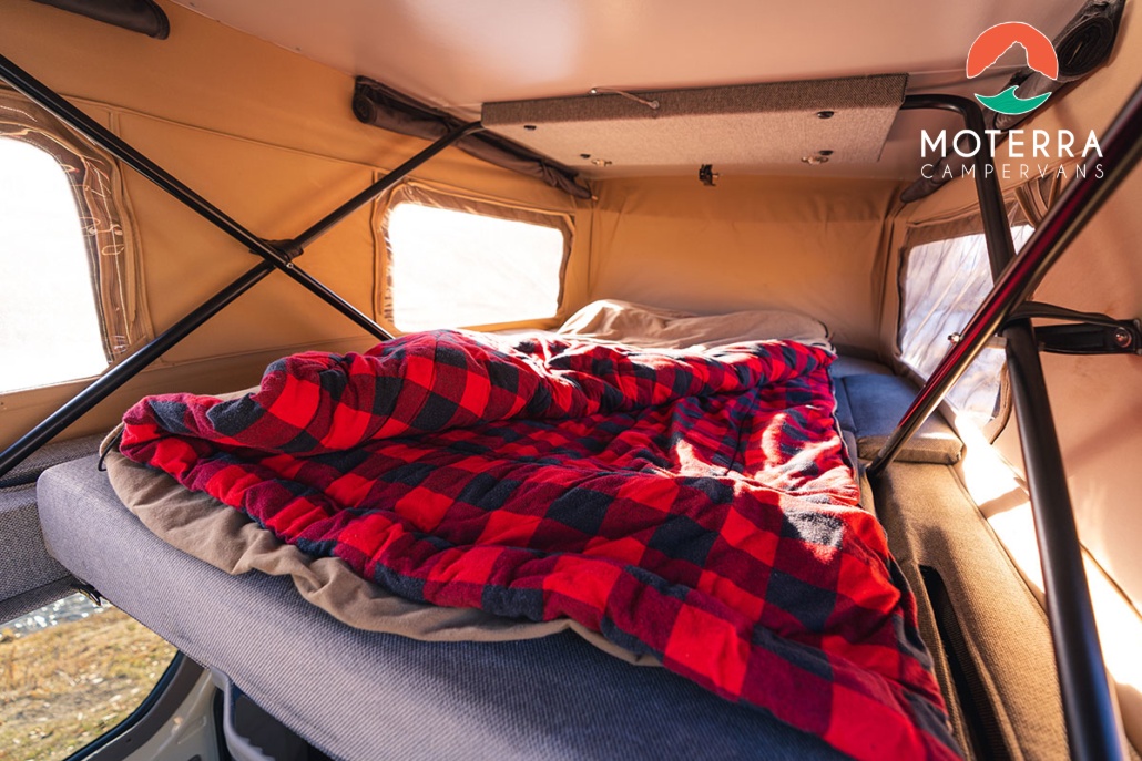 Cozy pop-top RV rental interior: a comfy bed with a red plaid blanket bathed in sunlight, ready for adventure.. Mercedes-Benz Sprinter 2020