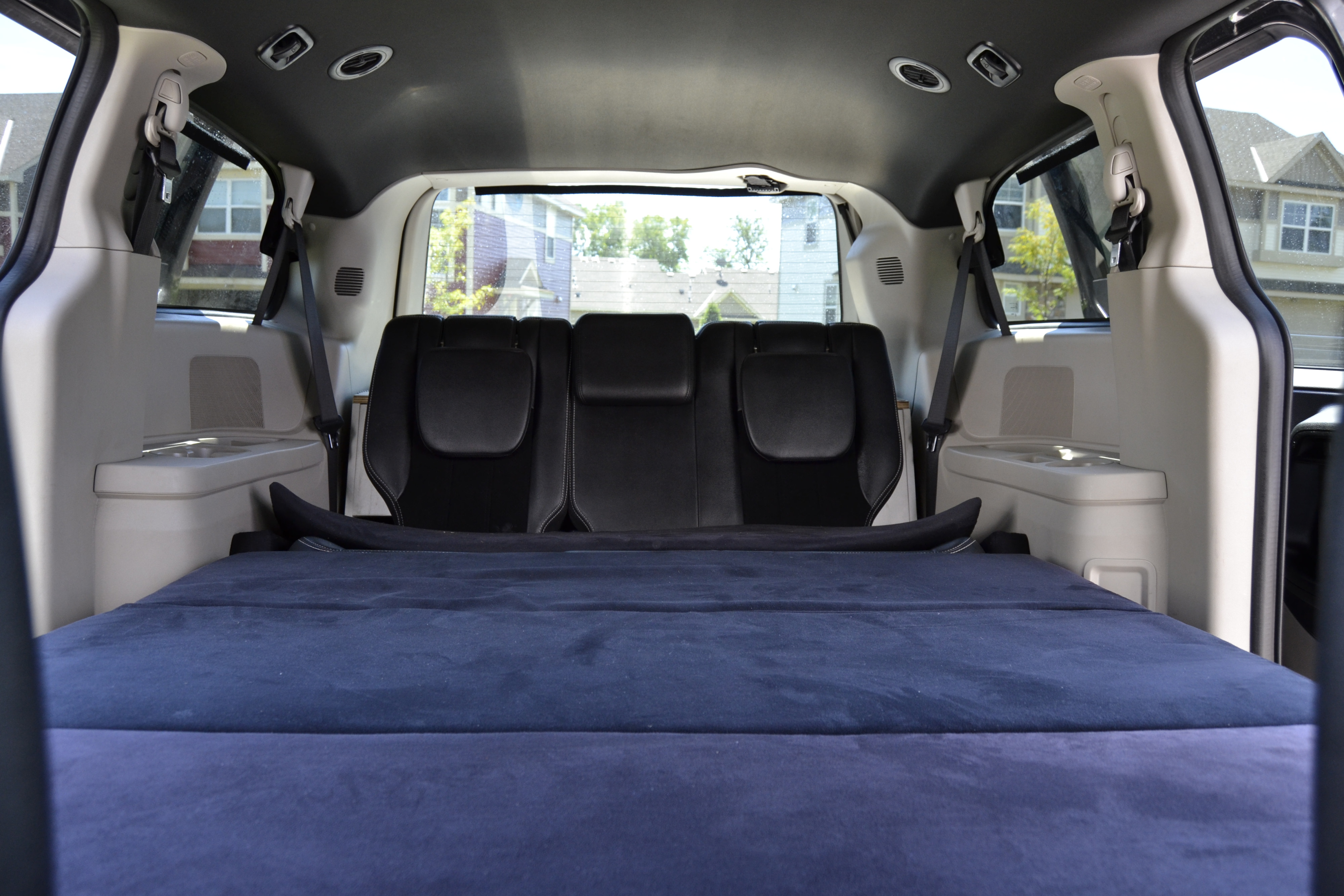 Cozy vehicle interior, perfect for an RV rental. Blue mattress laid over folded seats creates a comfy sleeping area.. Dodge Grand Caravan 2018