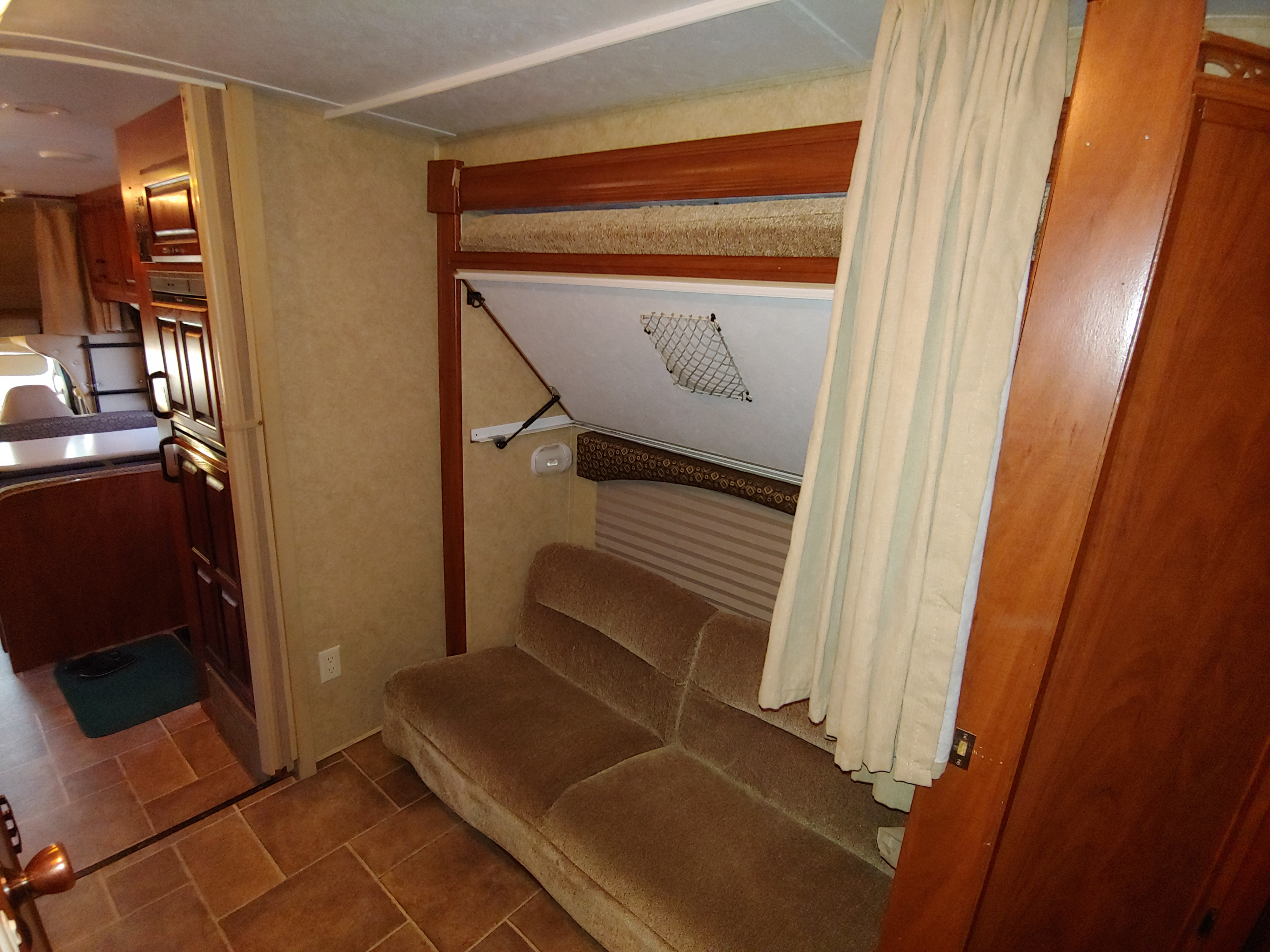 Cozy RV rental interior features a brown sofa, a fold-down bunk bed above, and a kitchenette in the background.. Forest River Sunseeker 2012