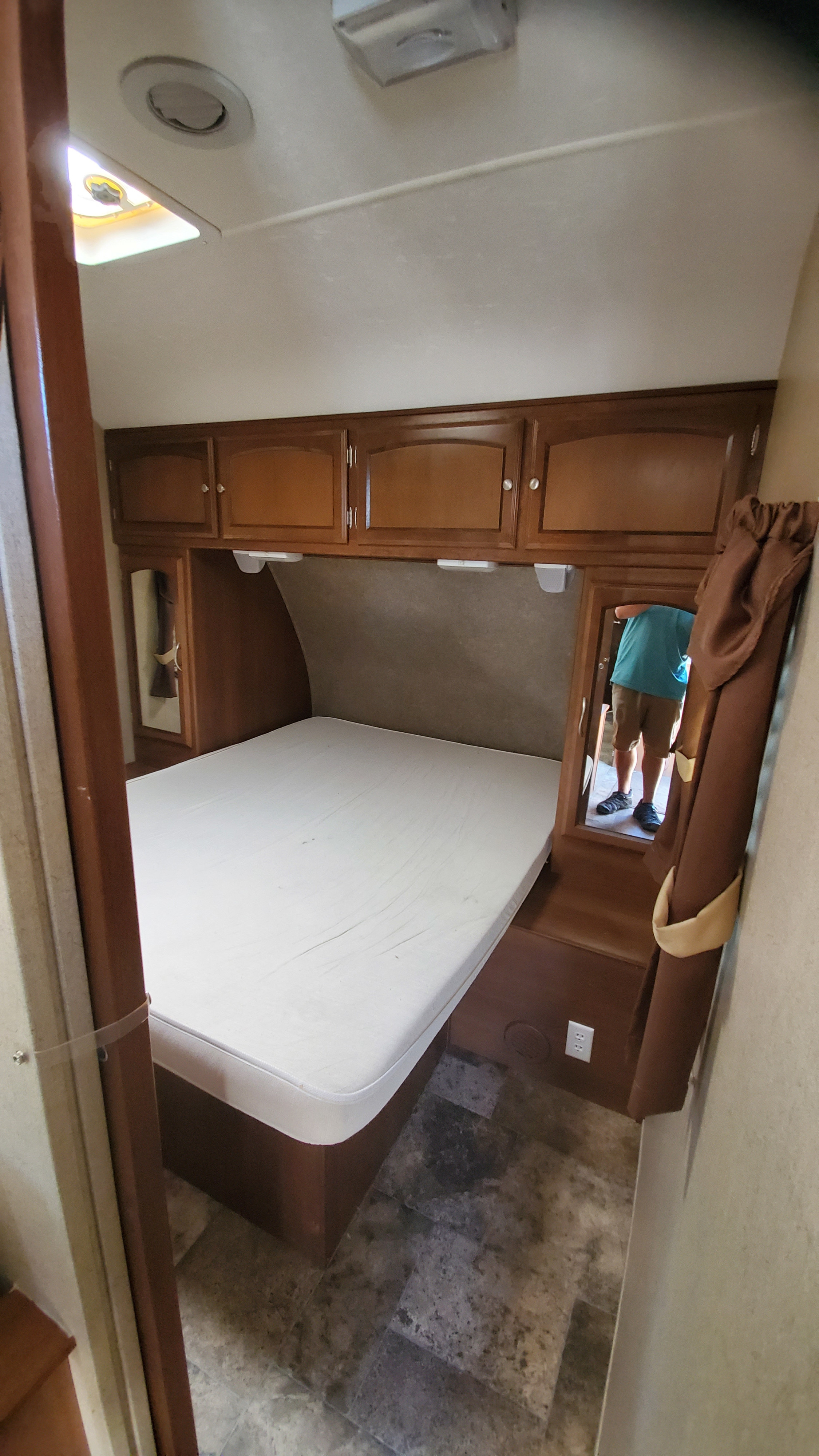 This RV rental's cozy bedroom features a bed, overhead cabinets, and mirrors. A compact and functional living space.. Coachmen Freedom Express 2015