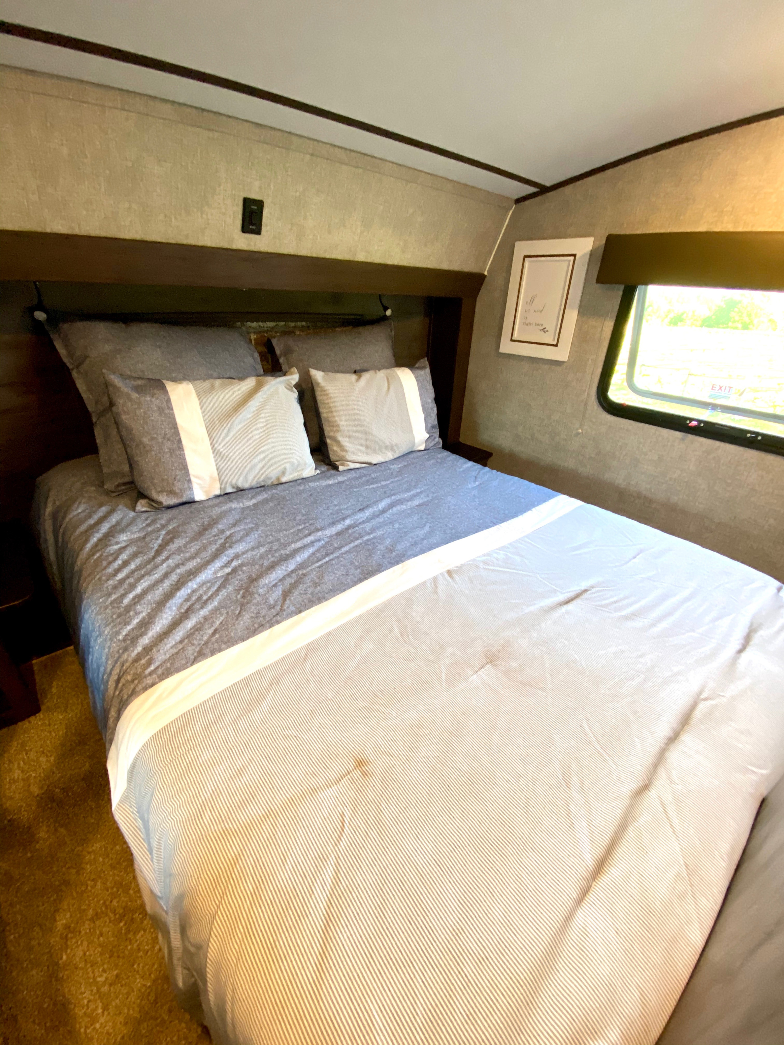 Comfortable RV rental bedroom with striped bedding, a cozy bed, and window view. Ideal for your travel accommodation.. Forest River Cherokee Arctic Wolf 2019