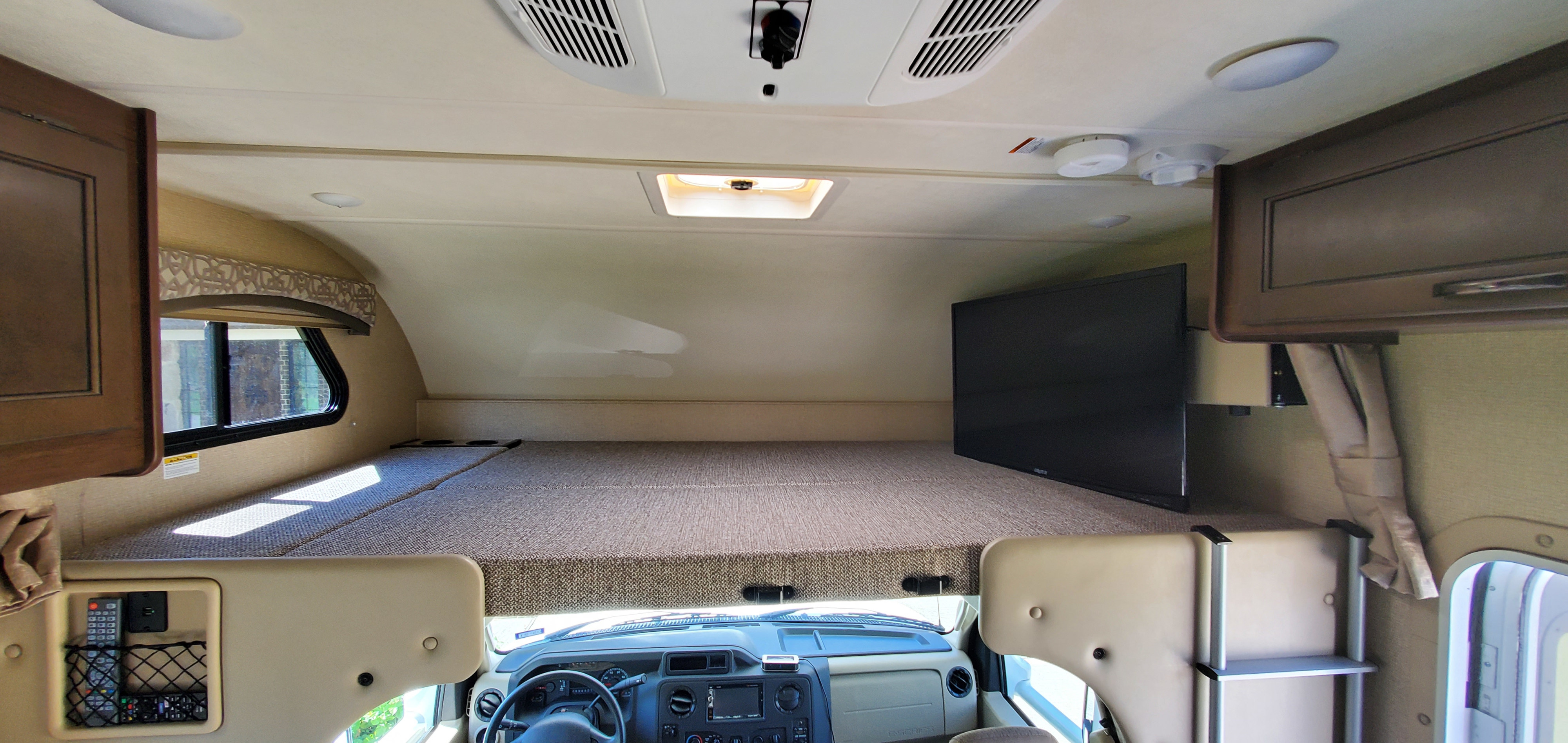 Inside an RV rental, showcasing the spacious cab-over bunk bed with mounted TV, and the driver's area below.. Thor Chateau 2019