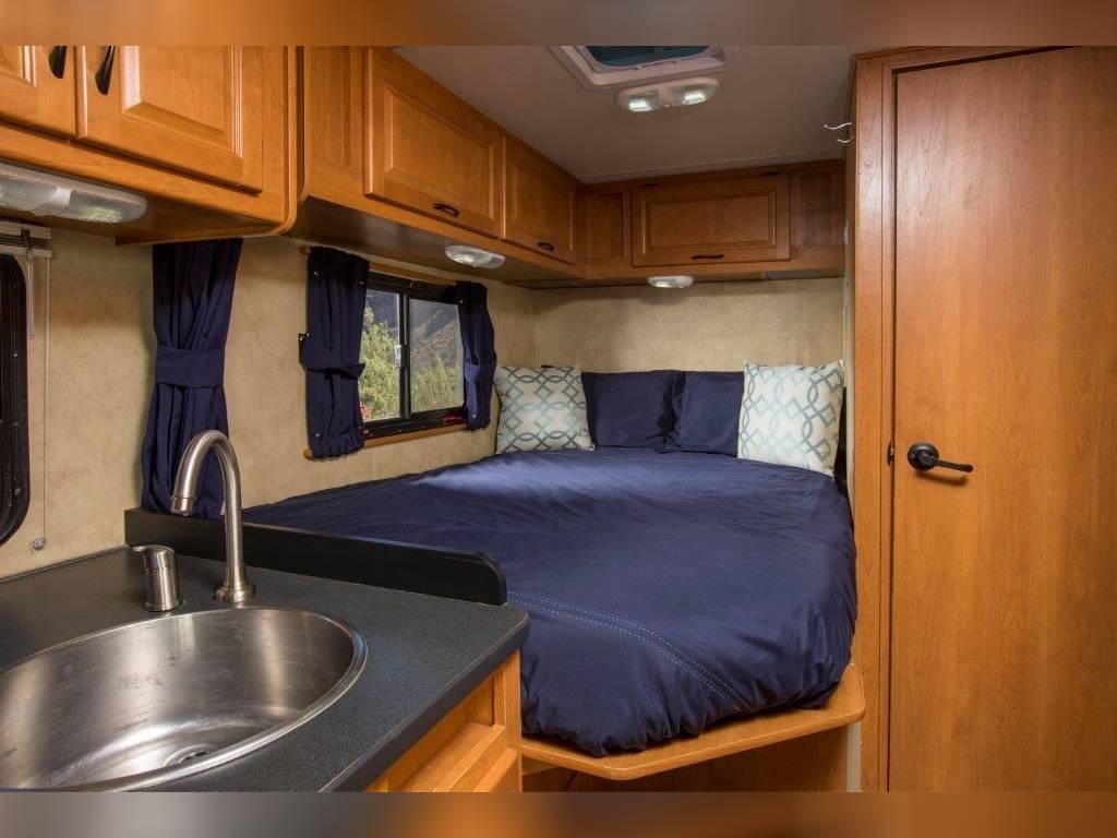This cozy RV rental interior features a compact bedroom area with a navy bed, alongside a small kitchen sink.. Thor Motor Coach Four Winds Majestic 2014
