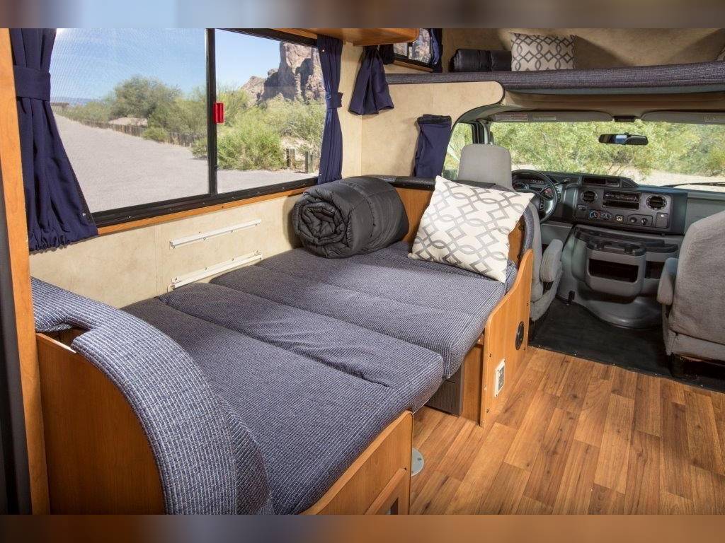 RV rental interior features a convertible bed, large window with desert view, and driver's cockpit. Ready for road trips.. Thor Motor Coach Four Winds Majestic 2014
