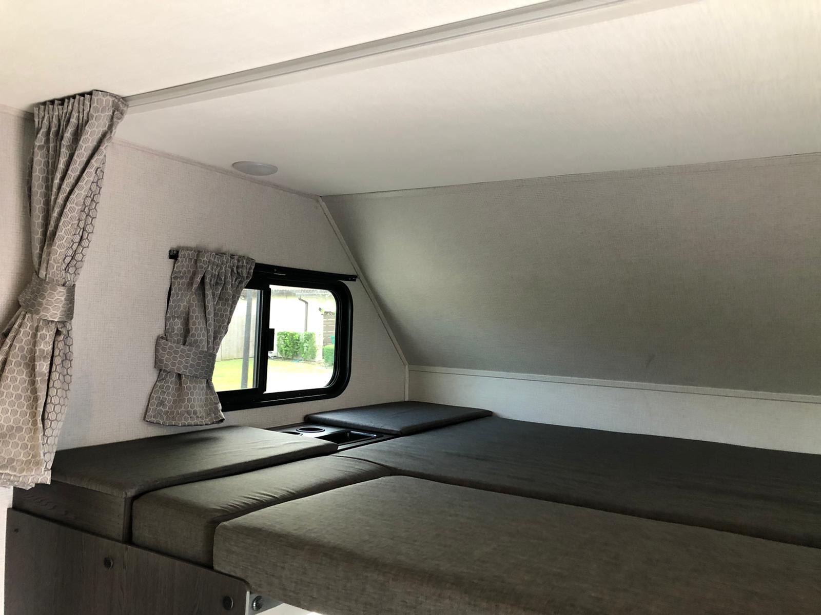 Inside this RV rental, find a compact sleeping area with gray cushions, patterned curtains, and a side window, ideal for road trips.. Ford E450 2020
