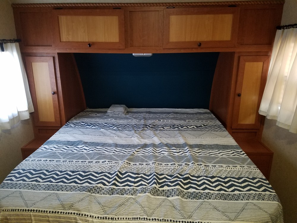 Cozy RV rental bedroom featuring a patterned bed, built-in wooden cabinets, and windows on both sides.. Gulf Stream Vista Cruiser 2015