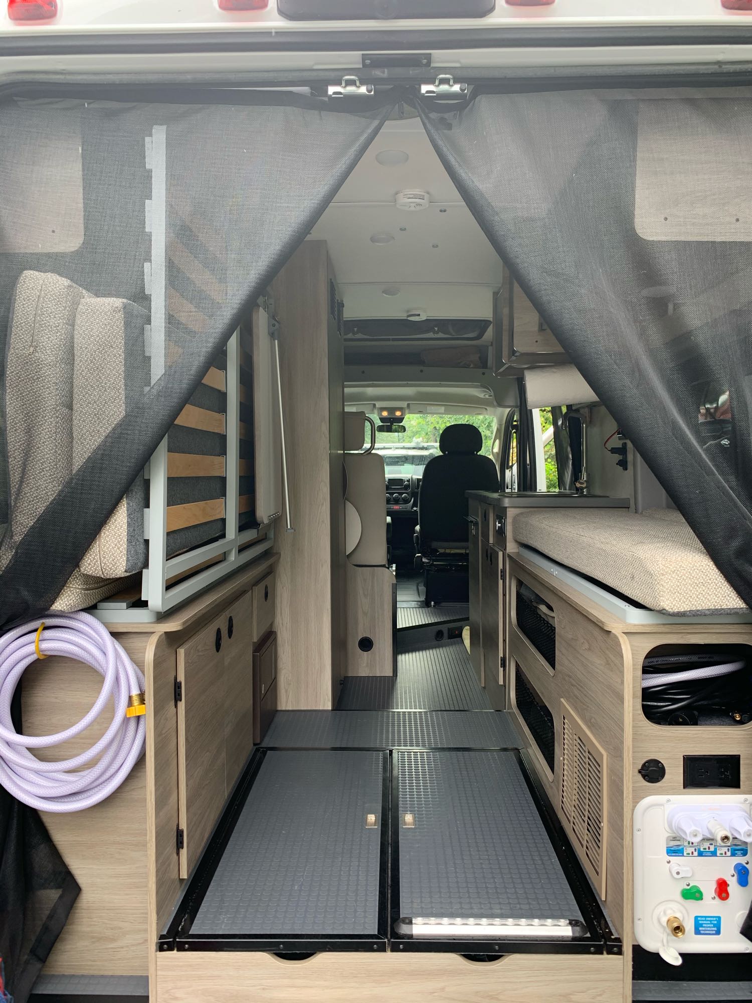 Inside an RV rental camper van: A view from the rear shows a compact interior with bed, kitchen, and utilities.. Winnebago Solis 59p 2020