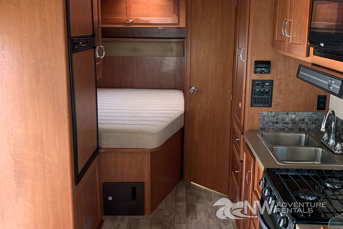 View inside an RV rental showing a bed, refrigerator, and kitchenette with sink and stove. Perfect for your next adventure.. Winnebago Spirit 2018