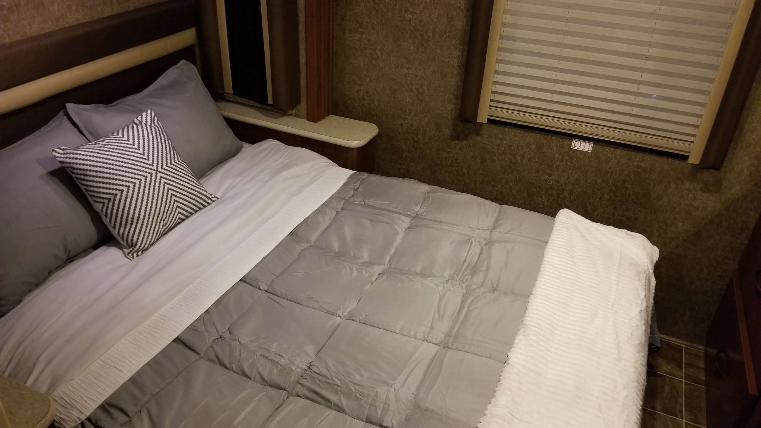 Cozy RV rental bedroom with a neatly made bed, grey bedding, and an accent pillow next to an exit window.. Thor Motor Coach A.C.E 2013