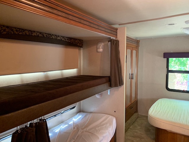 Cozy RV rental interior with dark brown bunk beds, white lower bunk, wardrobe, and additional sleeping area.. Jayco Redhawk 31X 2017