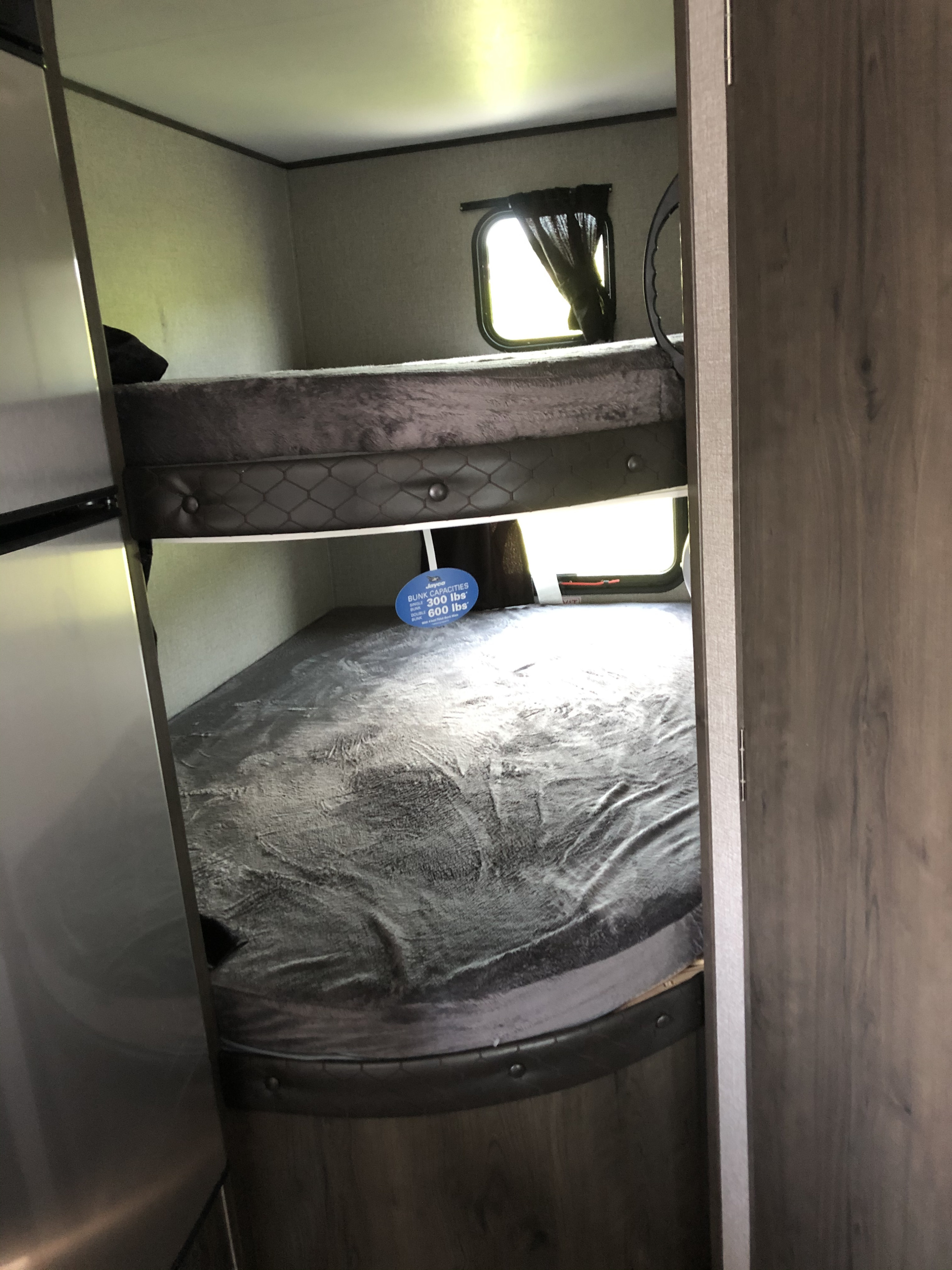 RV rental bunk beds, showing mattresses & windows. A sign details capacities: 300 lbs (single), 600 lbs (double).. Jayco Jay Flight 2021
