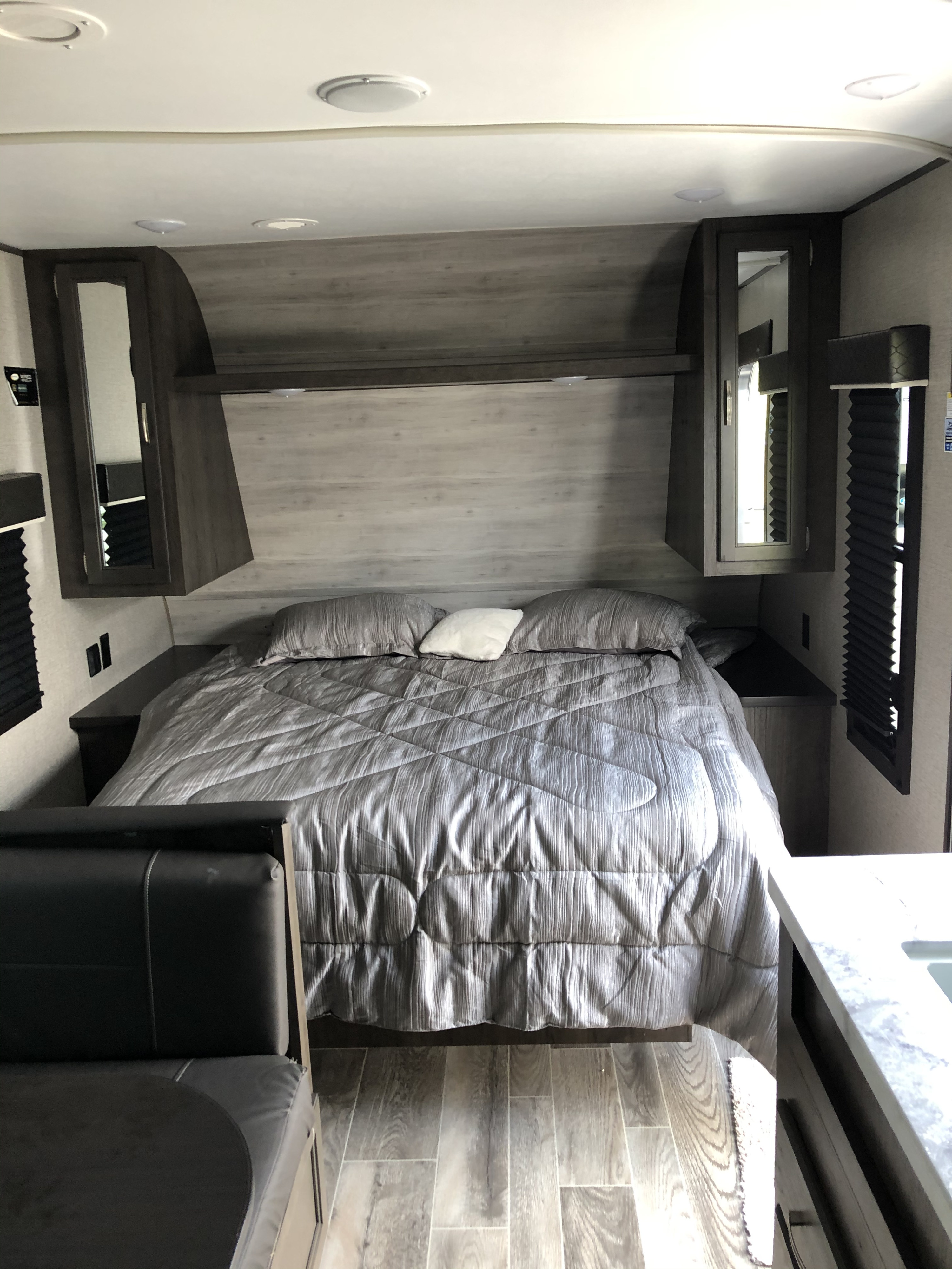 Inside this RV rental is a bedroom with a gray bed, mirrored overhead cabinets, and wood-patterned flooring.. Jayco Jay Flight 2021