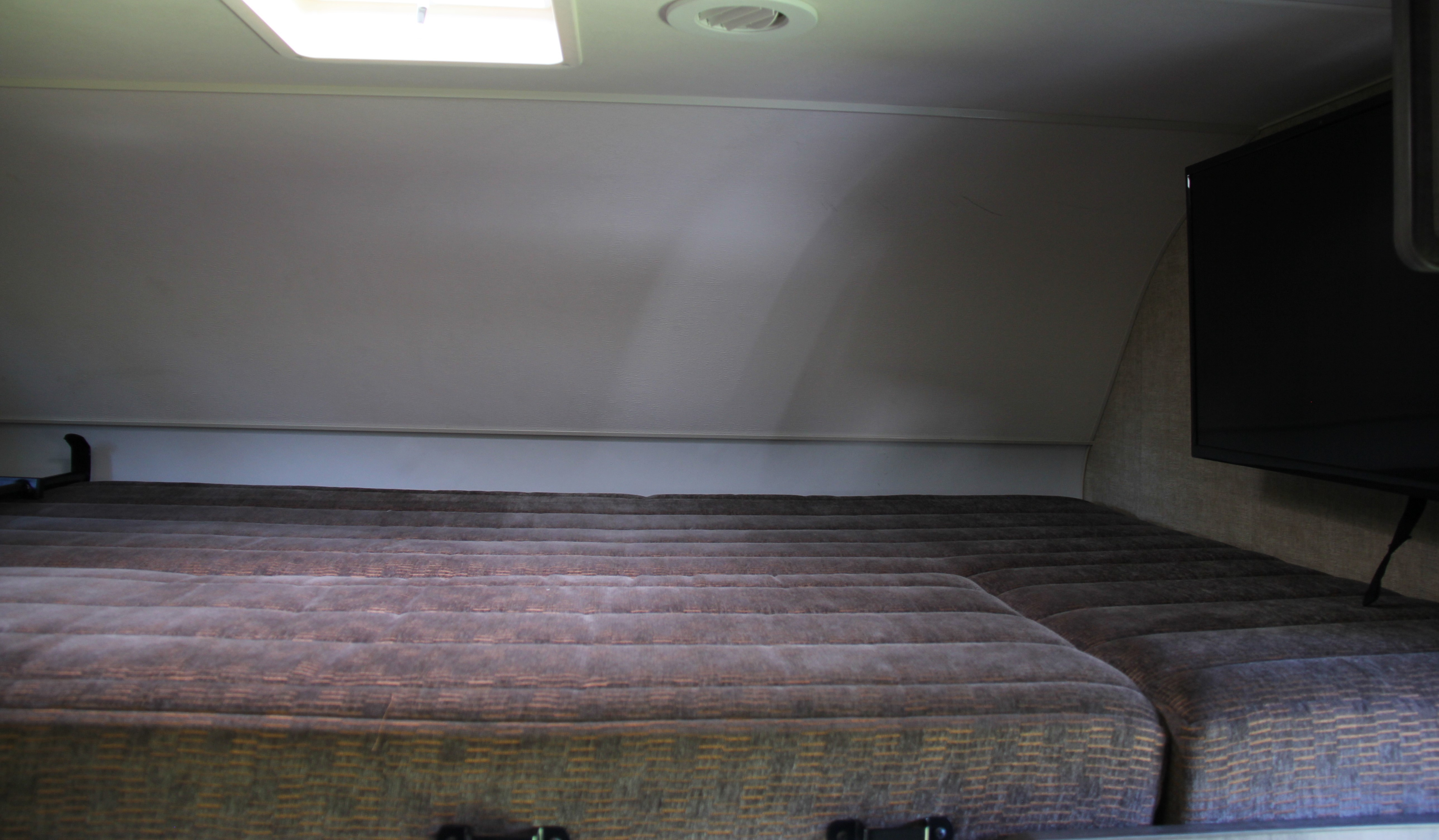 Cozy RV rental sleeping area with segmented mattress, overhead light, vent, and TV for comfortable travels.. Winnebago Minnie Winnie-Hook 2019