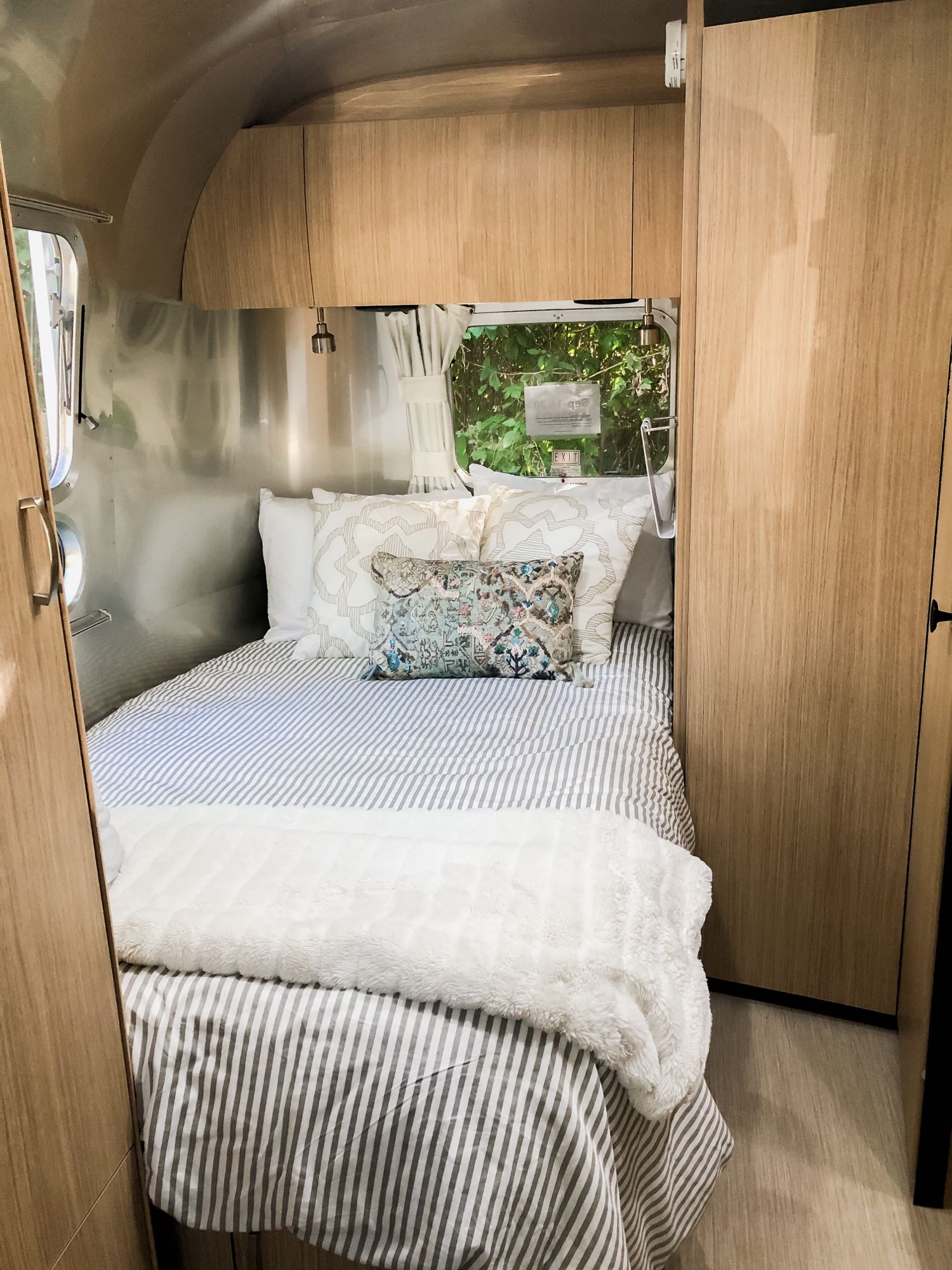 Step inside this cozy RV rental's bedroom, featuring a striped bed, plush blanket, and classic Airstream aluminum walls & wood accents.. Airstream Flying Cloud 2020