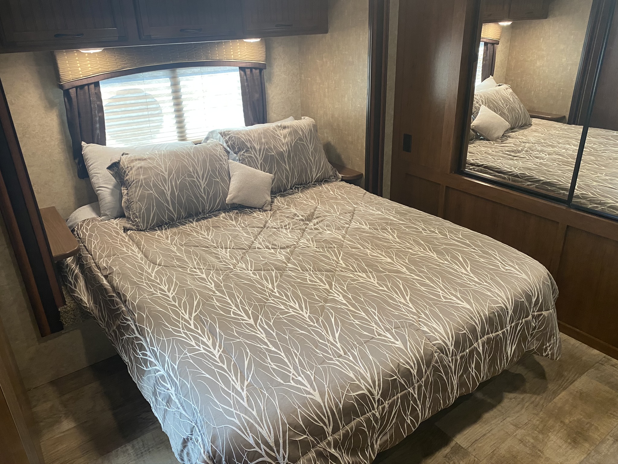 Cozy RV rental bedroom with a grey bed featuring a white branch pattern, overhead cabinets, and mirrored closet.. Jayco White Hawk 2017