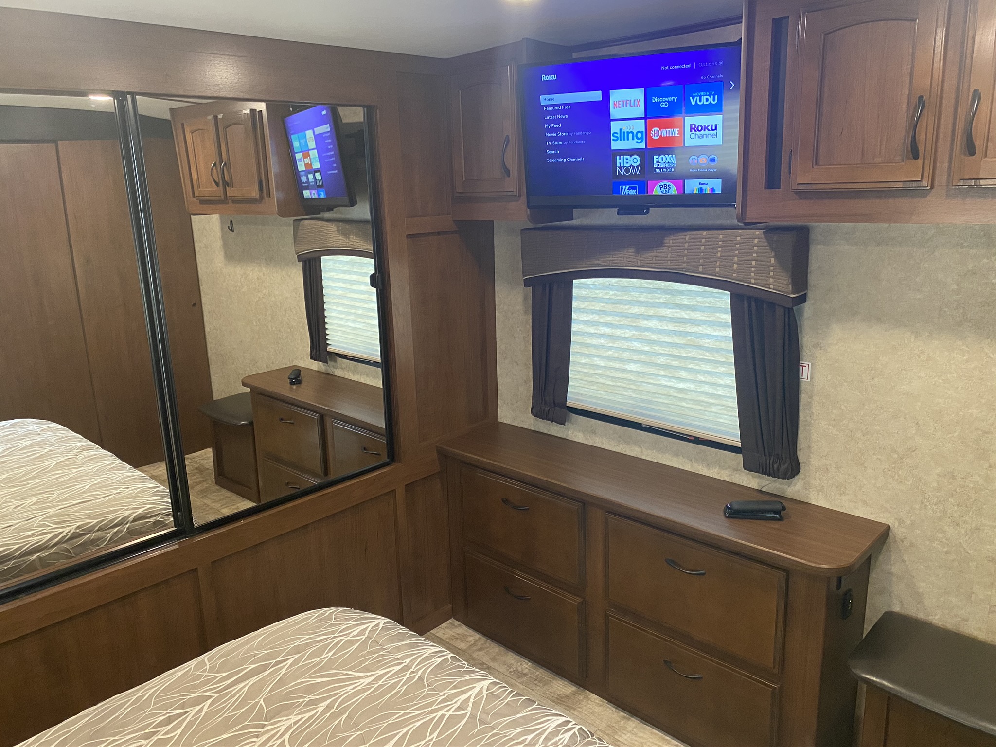 RV rental bedroom showcasing a comfortable bed, large mirror, storage, and a wall-mounted Roku TV for entertainment.. Jayco White Hawk 2017