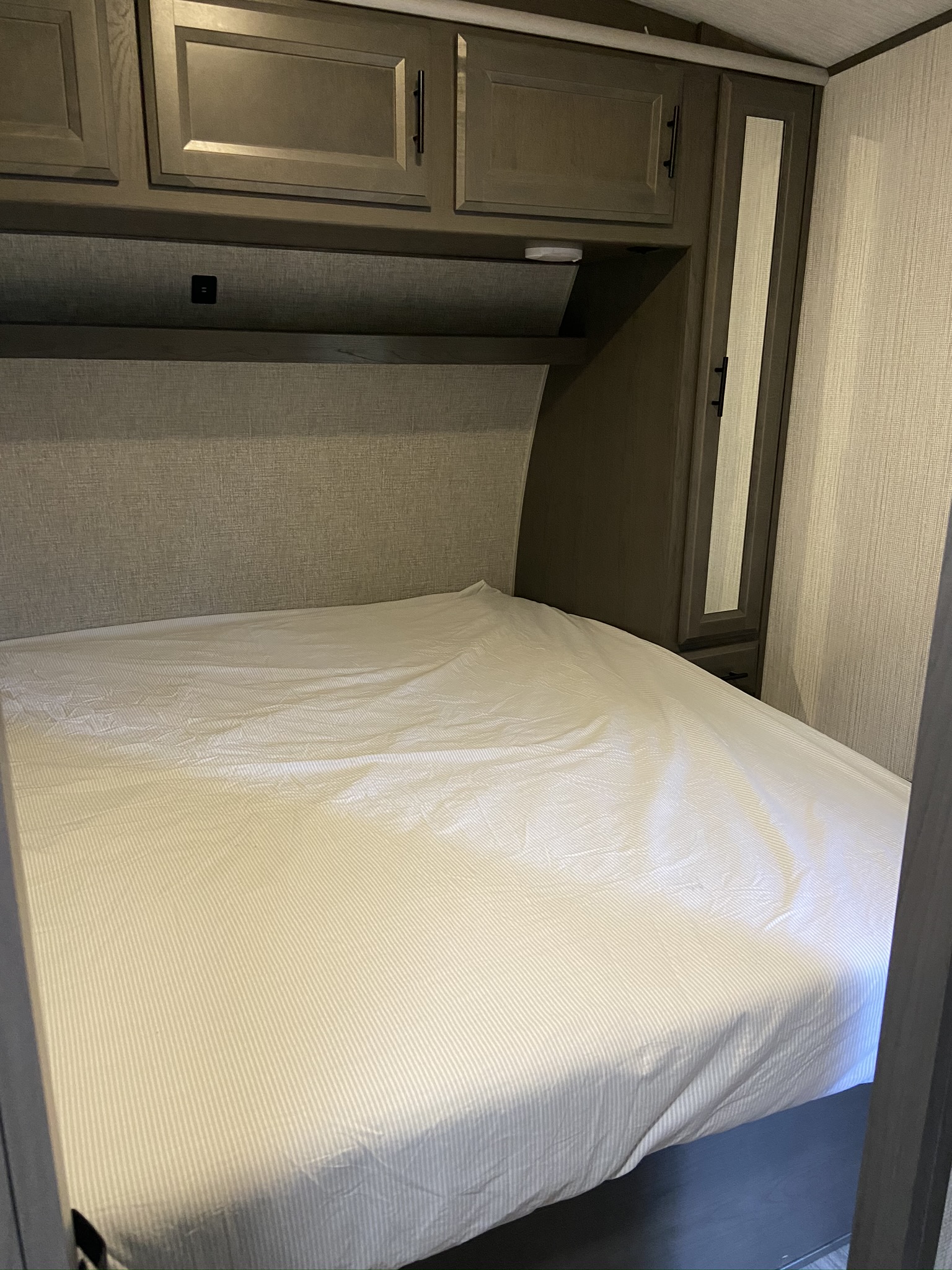 This RV rental bedroom features a striped bed, overhead cabinets, a charging port, and a mirrored wardrobe.. Heartland Fuel 250 2021