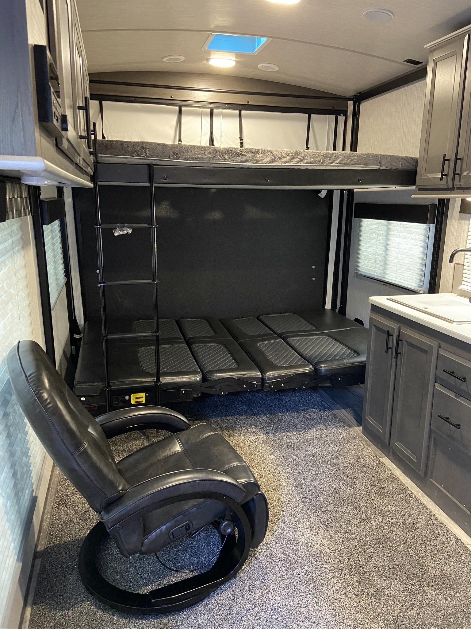 Inside an rv rental, showing a multi-purpose living area with an upper bunk bed, lower convertible sofa, and leather recliner.. Heartland Fuel 250 2021