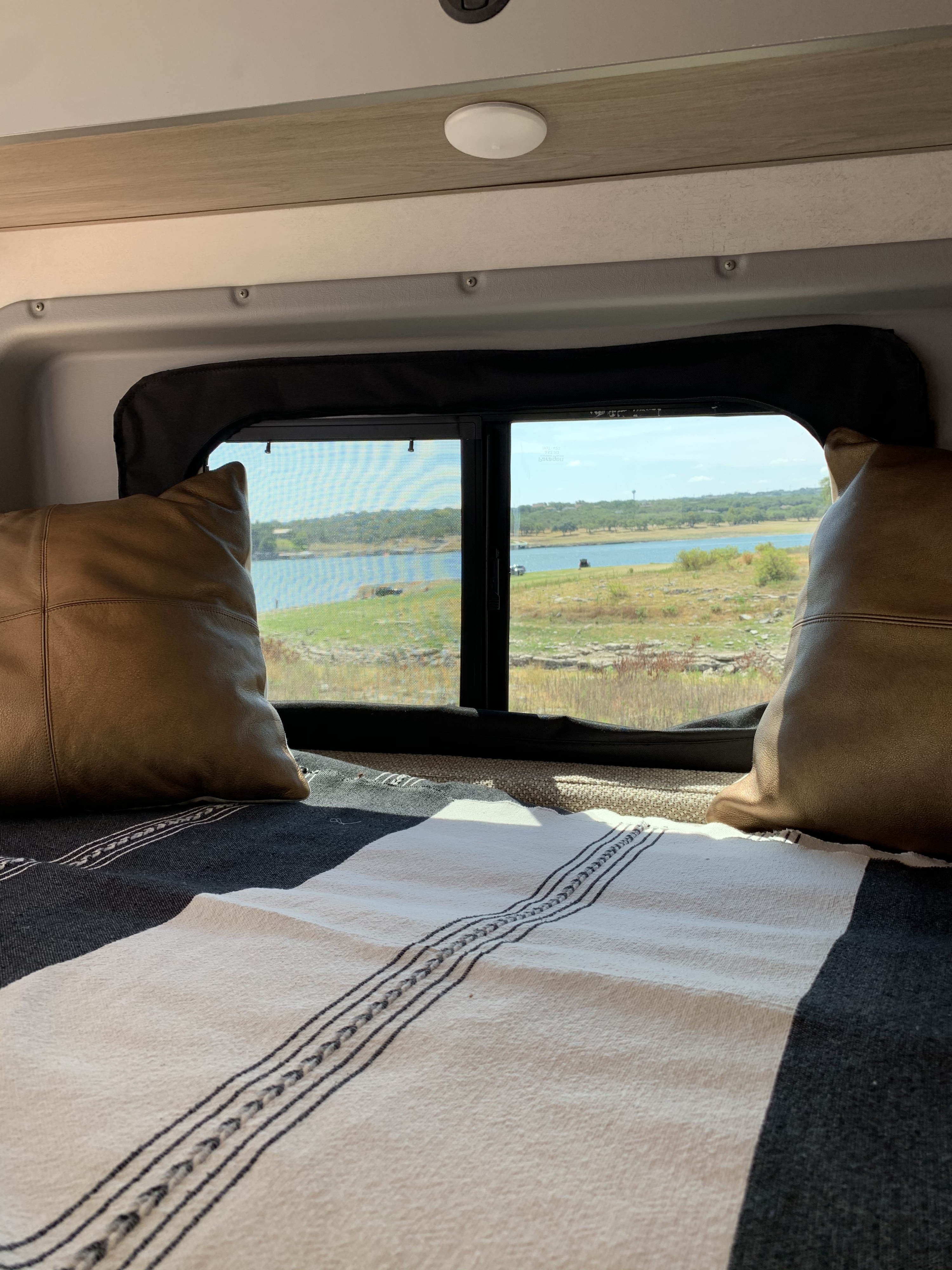 Comfortable RV rental bed with a scenic window view of a serene lake and natural landscape, ideal for travelers.. Winnebago Solis 2021