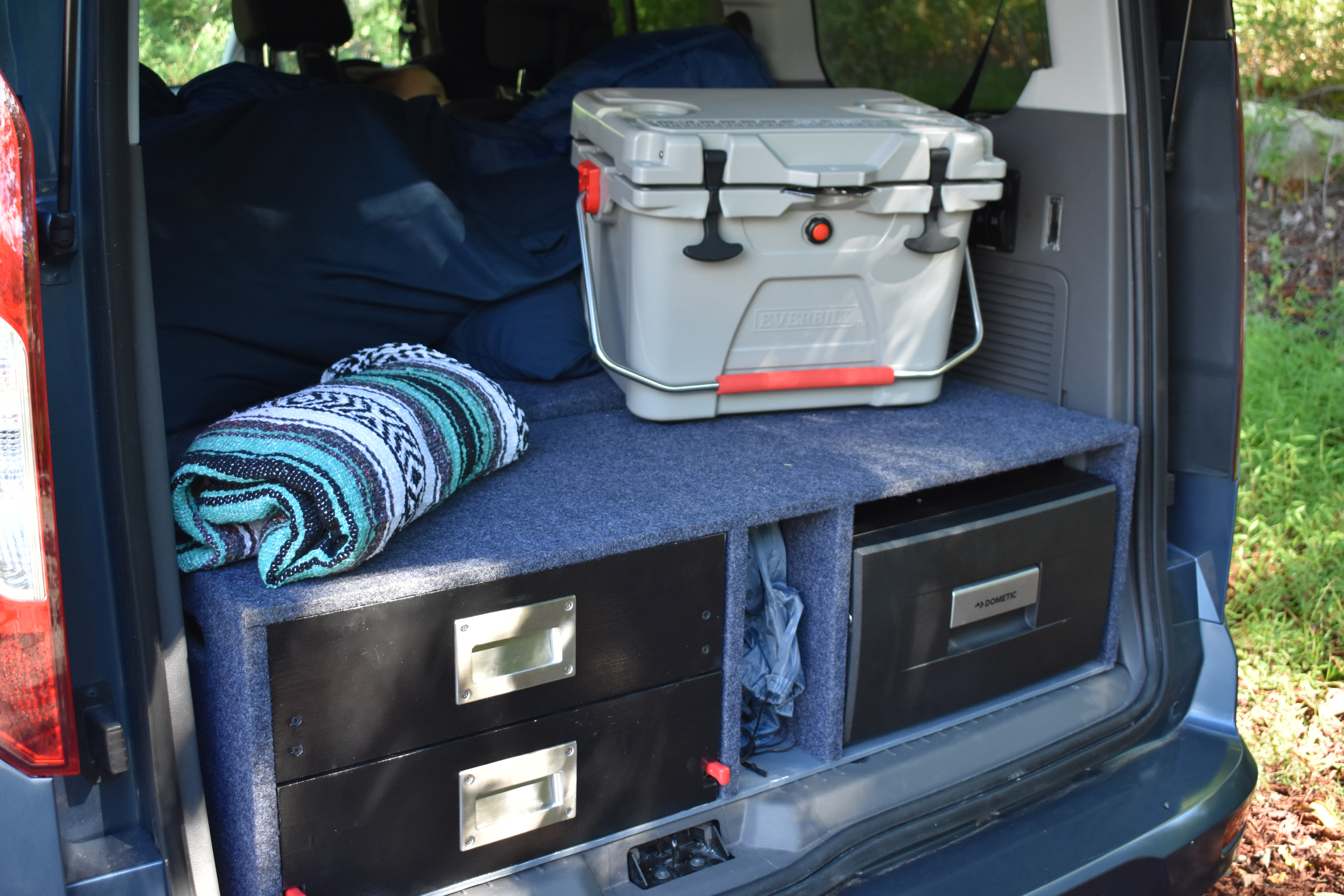 Custom van storage for an RV rental: a cooler, Dometic fridge, and drawers on a carpeted platform with a sleeping area.. Ford Van 2019