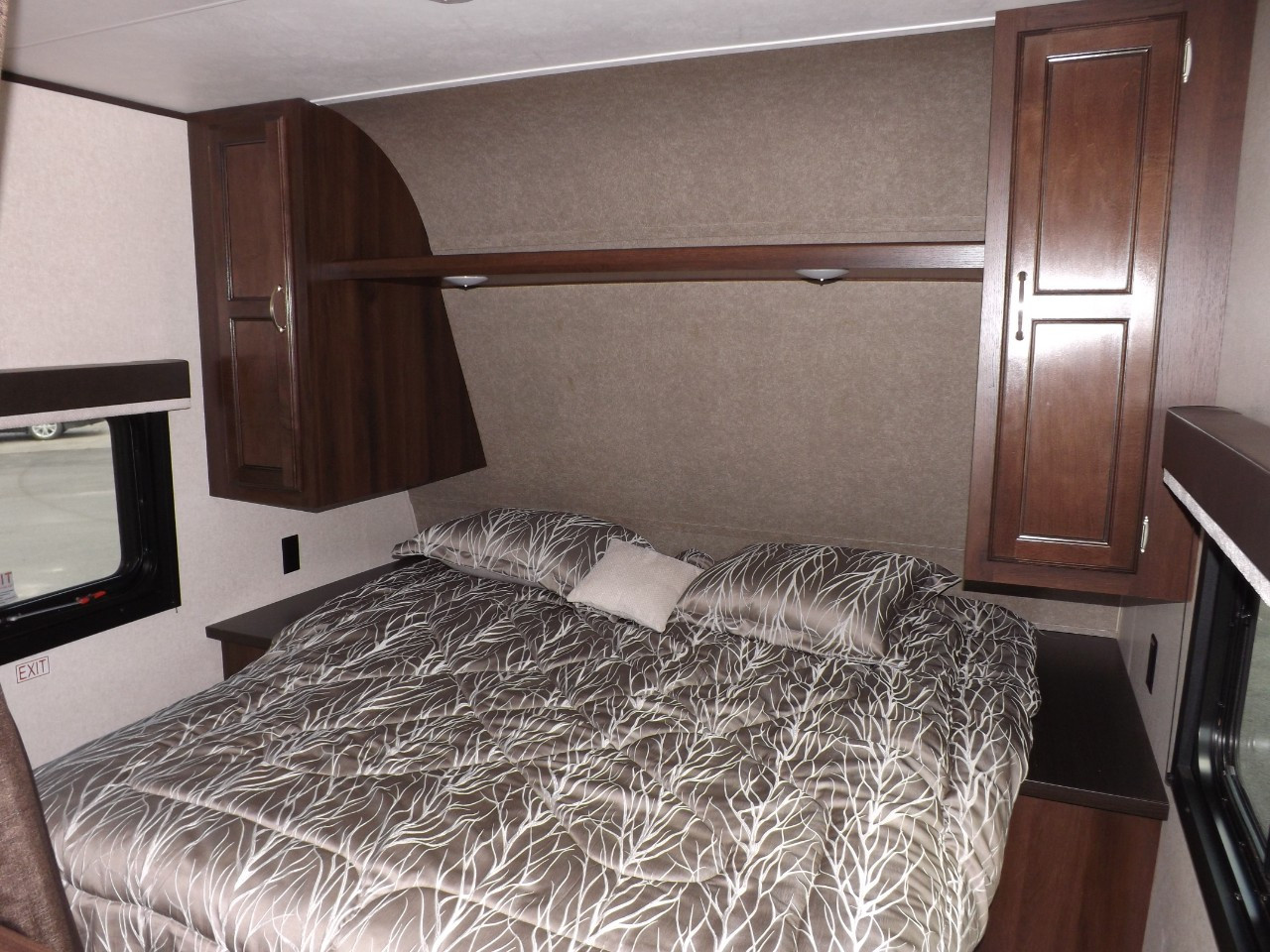 Comfortable RV rental bedroom with a full bed, patterned bedding, dark wood cabinets, and windows.. Jayco Jay Flight 2018