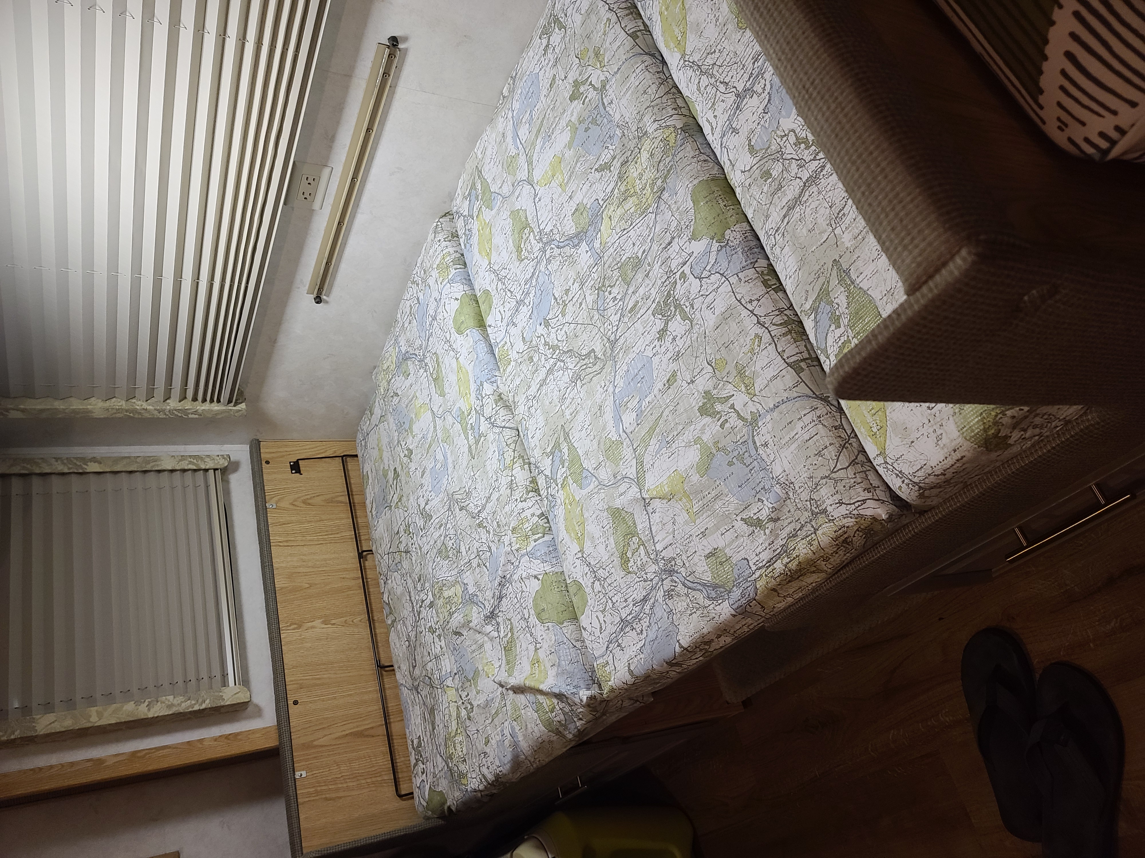 RV rental sleeping area featuring map-patterned bedding, vertical blinds, and wood paneling.. Fleetwood Bounder 2002