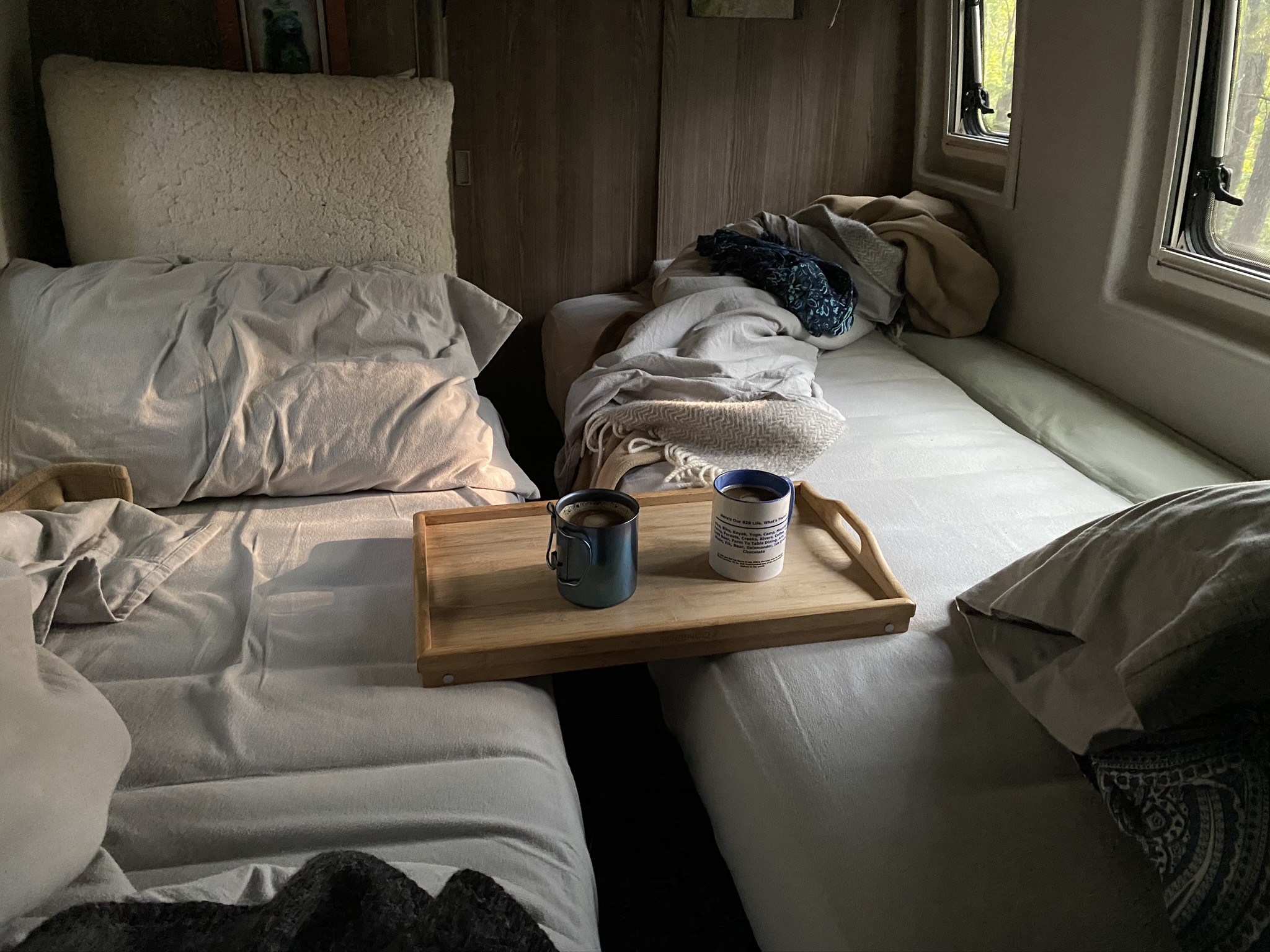 Cozy rv rental interior with two beds, featuring a wooden tray with coffee mugs and windows showing trees outside.. Mercedes-Benz Boldt 2020