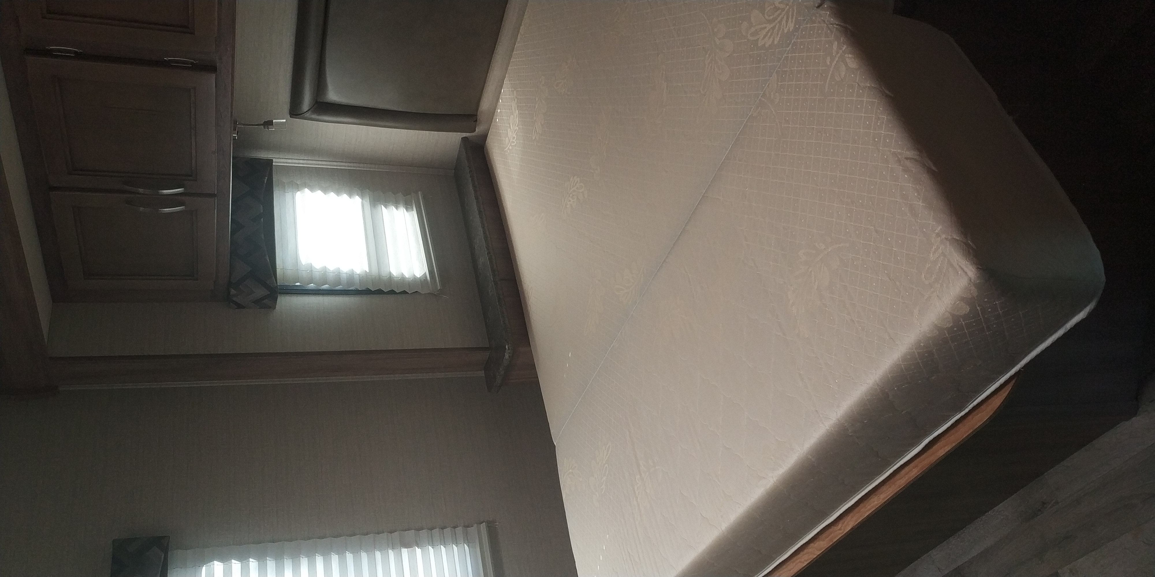 Bedroom in an RV rental featuring a large mattress, window with blinds, and built-in wood cabinets.. Jayco Redhawk 2020