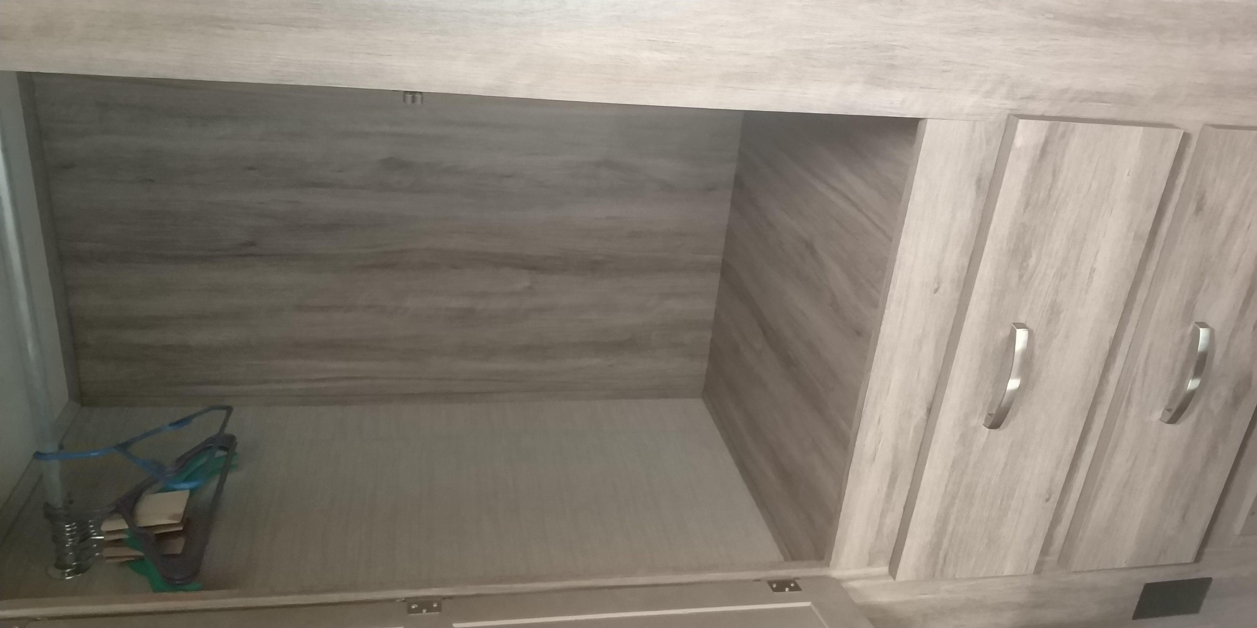 Spacious RV rental storage compartment with light wood paneling and two cabinet doors. Hangers rest on the floor.. Jayco Redhawk 2020