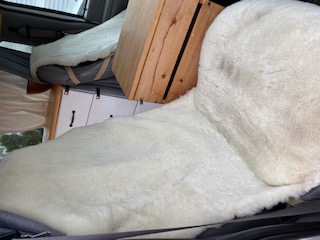 Cozy RV rental interior: plush white sheepskin on a campervan bed/seat, with practical wood crate and cabinets.. Ford Econoline E250supercab 1999