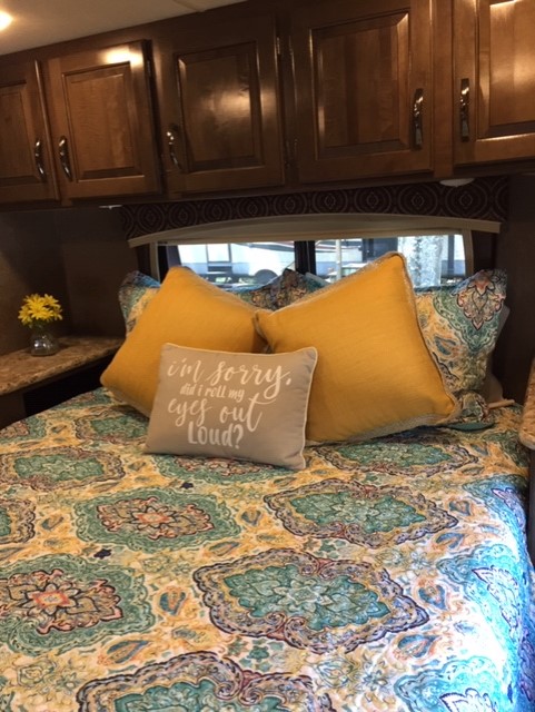 Bright RV rental bedroom featuring a bed with a colorful patterned quilt, yellow pillows, wood cabinets, and window. Cozy interior.. Thor Chateau 2017