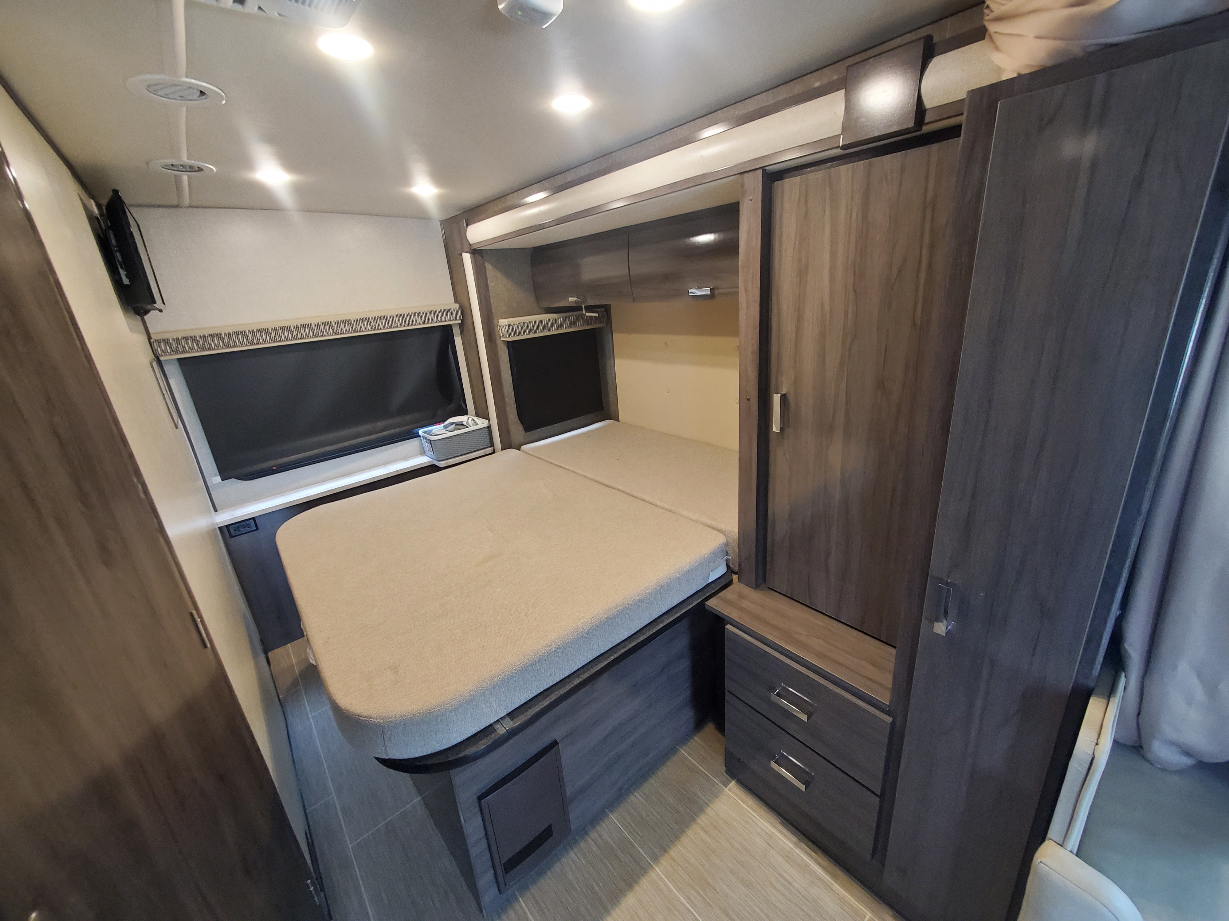 This RV rental bedroom offers a cozy bed, wall-mounted TV, storage cabinets, and window blinds. Ideal for comfortable travel.. Fleetwood Pulse 2019