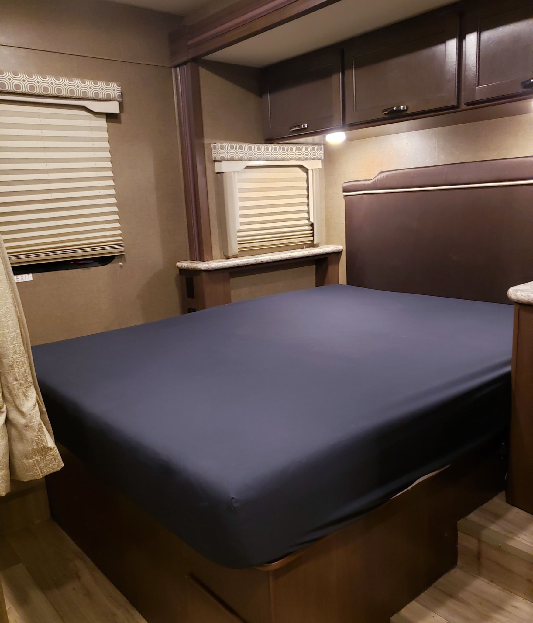 Cozy RV rental bedroom showing a bed, padded headboard, overhead cabinets, and window blinds for a mobile living space.. Thor Four Winds 2020