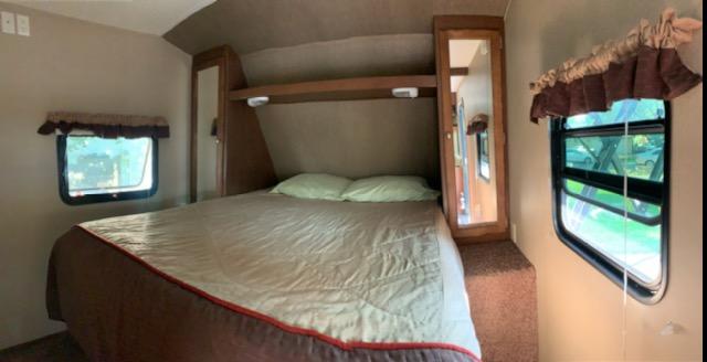 Cozy RV rental bedroom interior with a large bed, side closets (one mirrored), and bright windows. Ideal for travel lodging.. Dutchmen Aspen Trail 2015