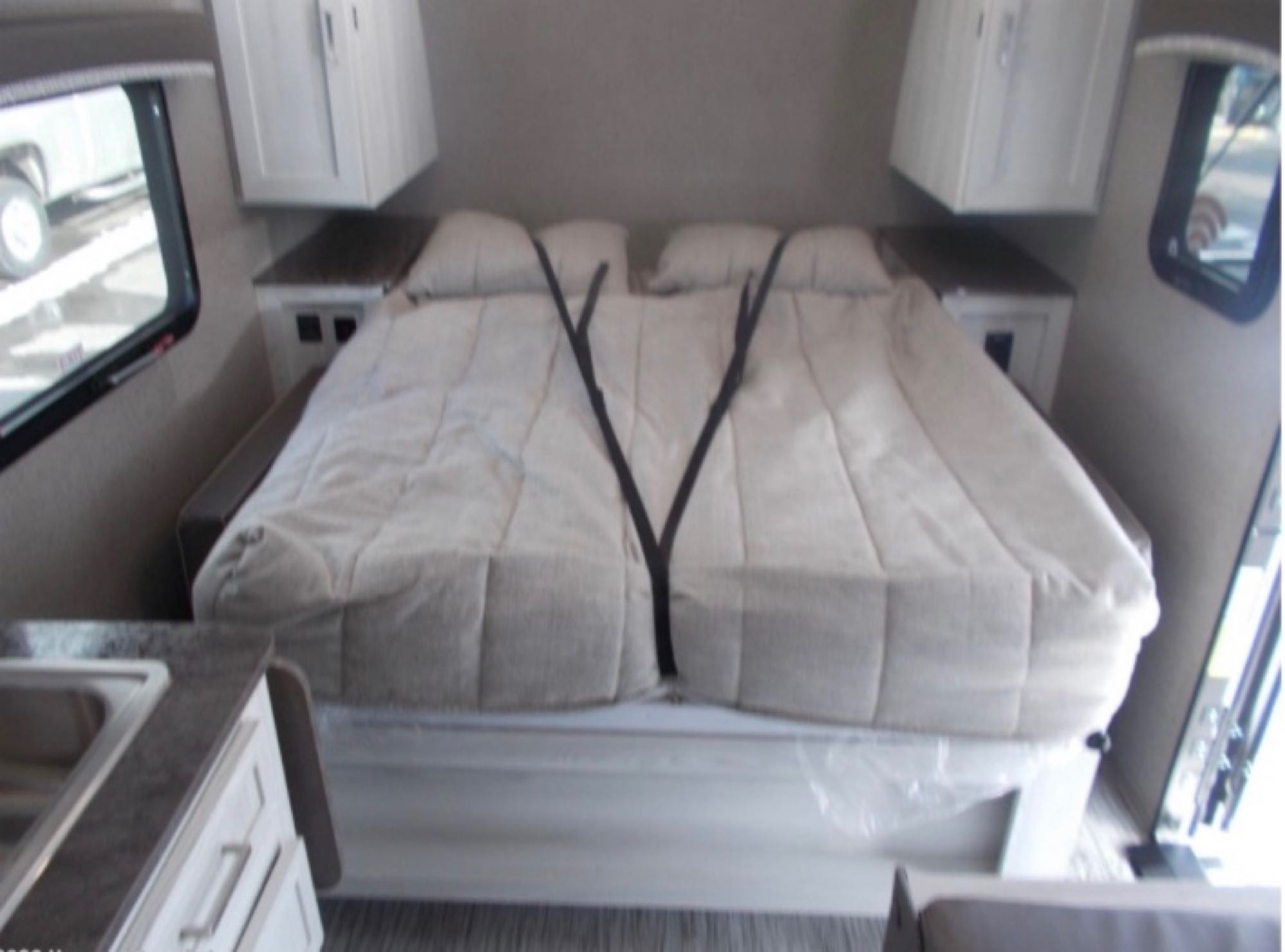 Interior of an rv rental showing a neat bedroom area with a bed, two pillows, side tables, and overhead cabinets.. Forest River Rockwood Geo Pro 2021