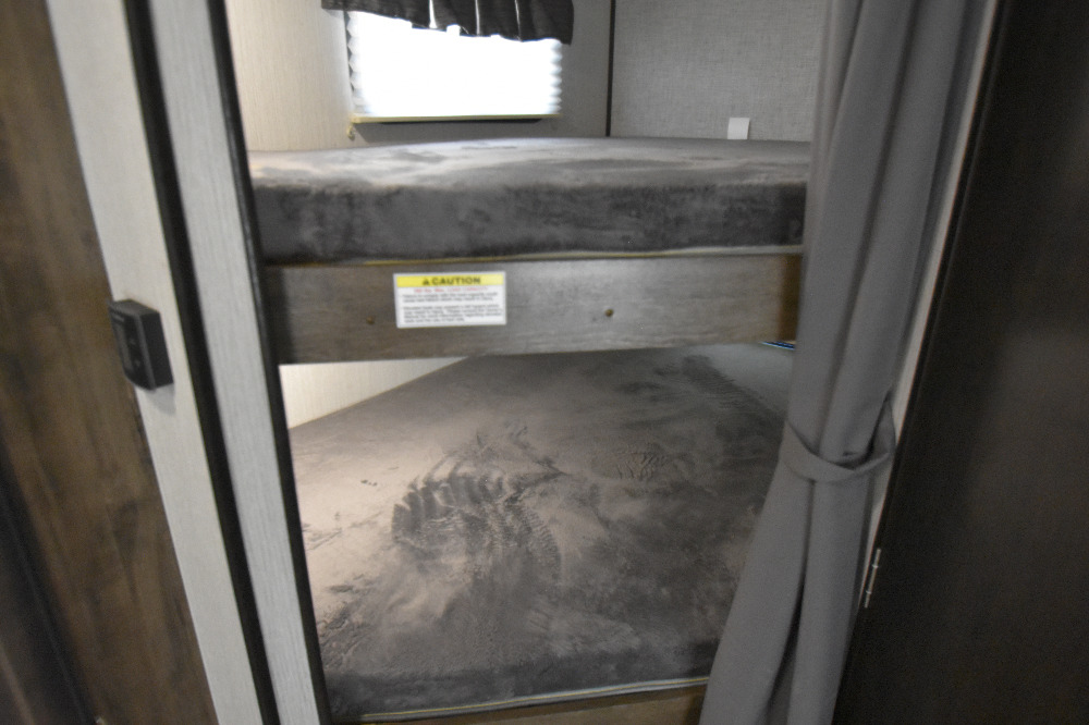 Inside an RV rental: two cozy bunk beds with soft gray mattresses, ideal for family adventures. A caution label is visible on the upper bunk.. Other Other 2020