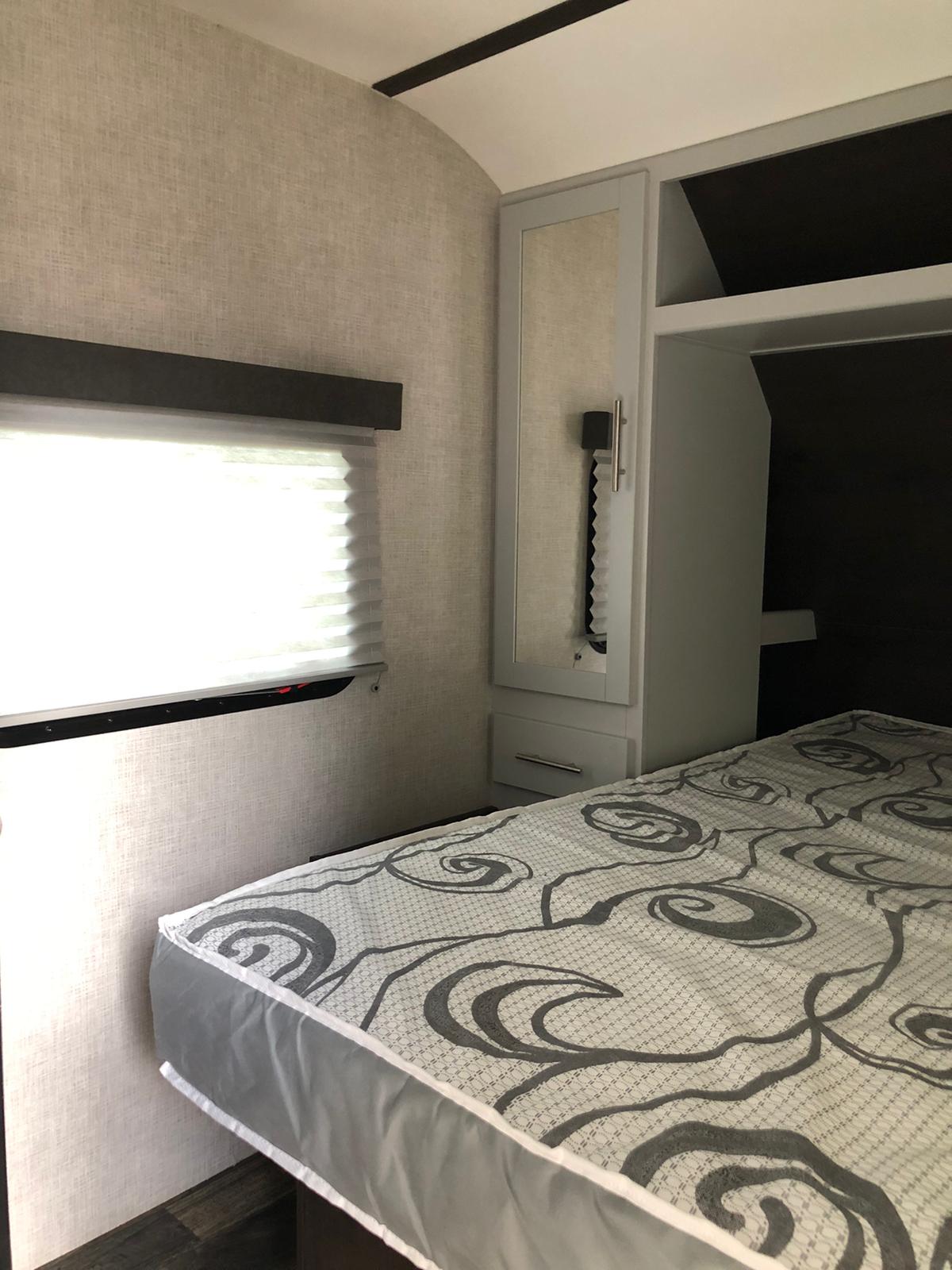 A cozy RV rental bedroom interior featuring a bed, window with blinds, and built-in storage cabinets.. Keystone Bullet 2020