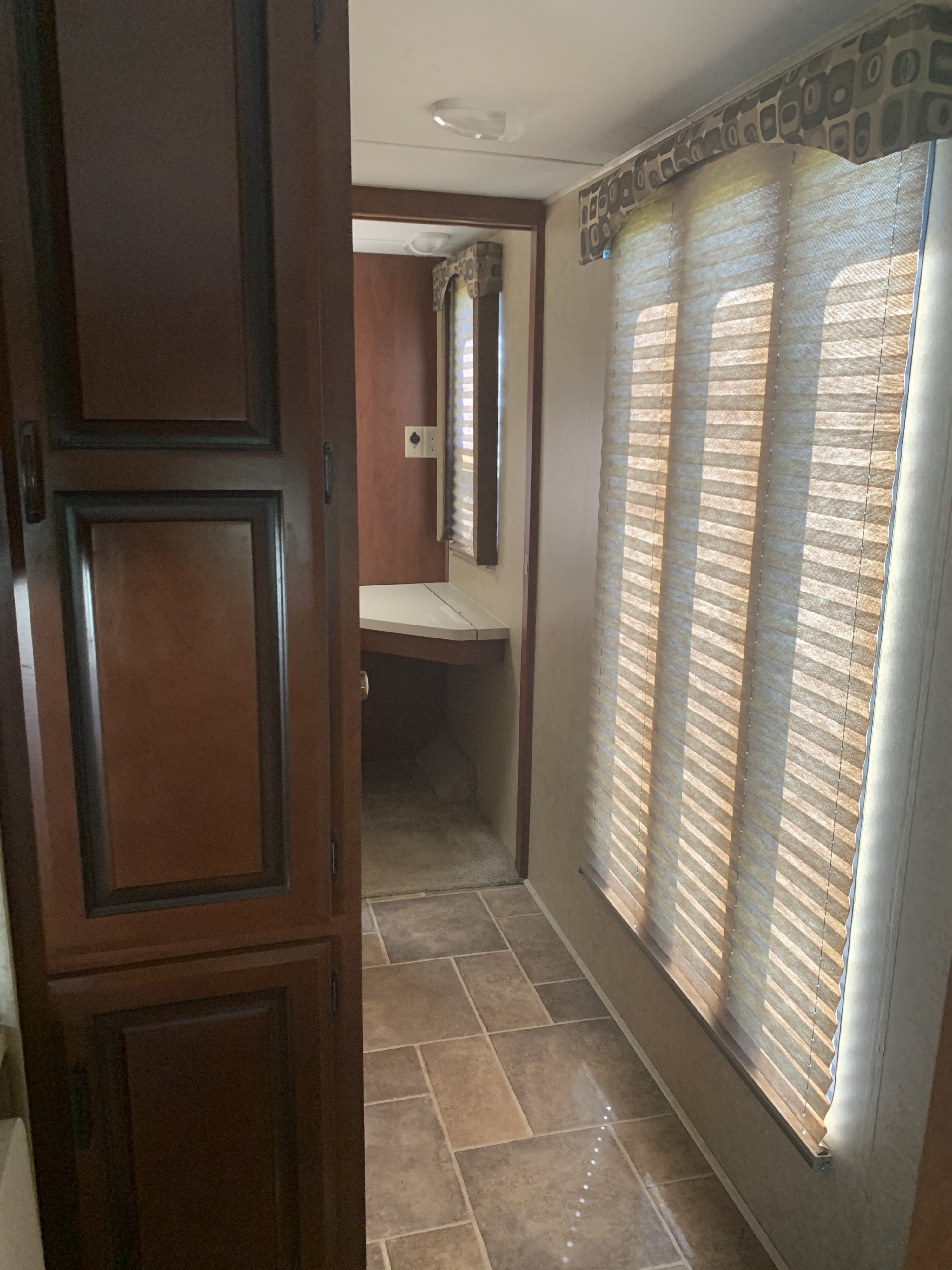Inside an RV rental, a narrow passage leads past wood cabinets, a sunlit window with blinds, to a small desk.. Forest River Sunseeker 2012