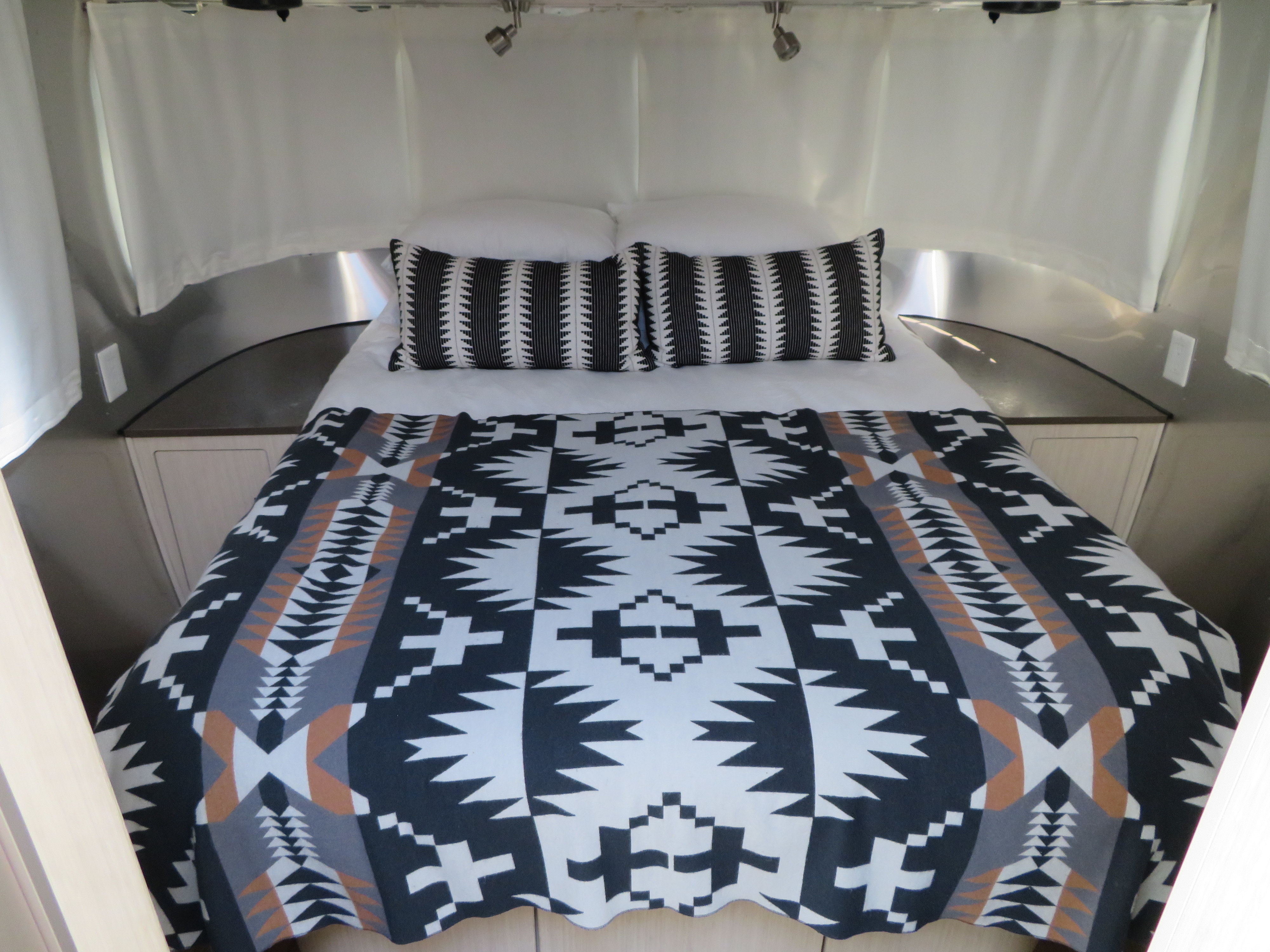 RV rental bedroom with cozy, patterned bedding inside a sleek aluminum interior, offering comfort on the road.. Airstream International 2017