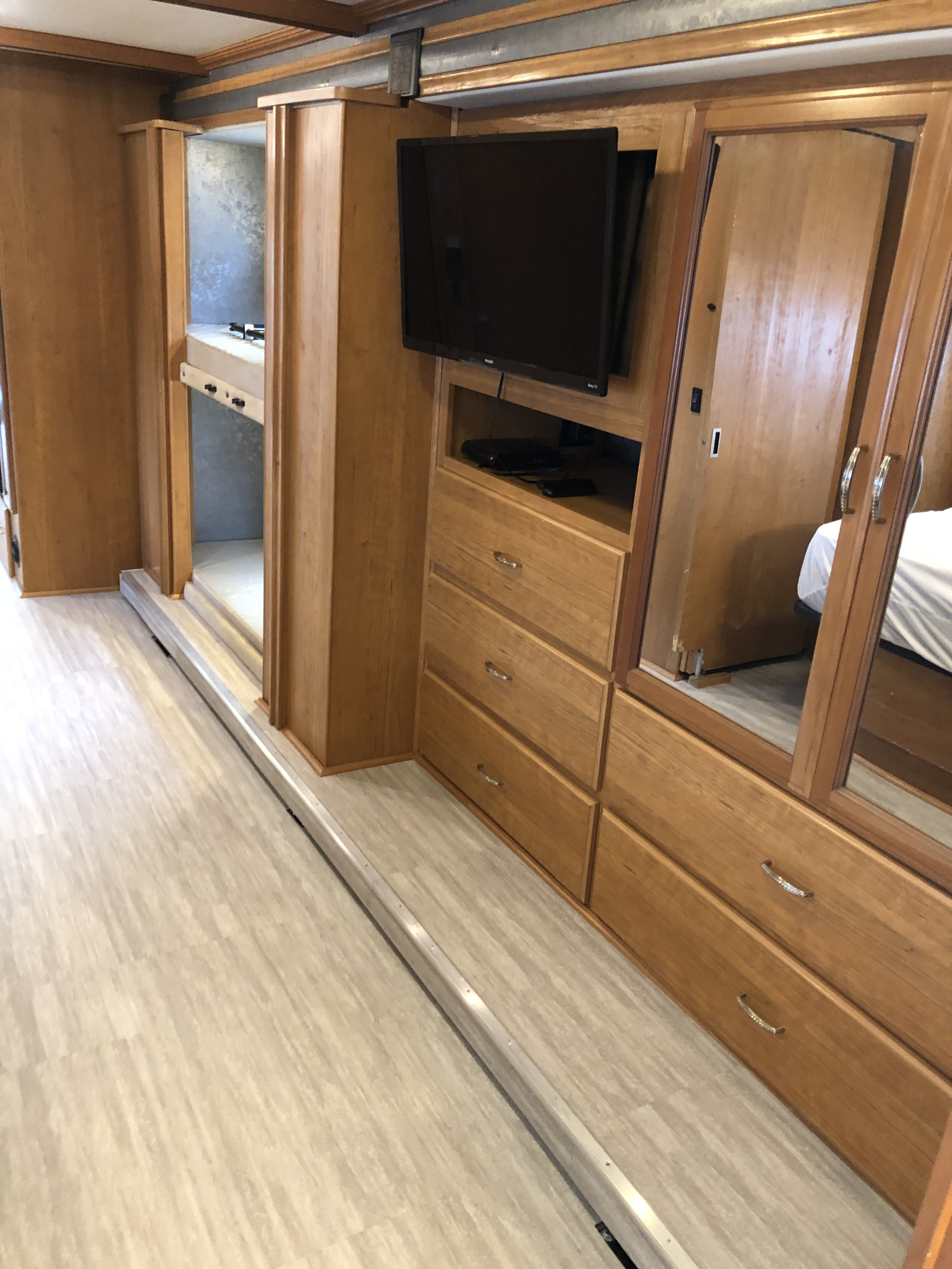 An RV rental interior featuring light wood cabinetry, a TV, storage drawers, a mirrored closet, and compact bunk beds.. Fleetwood Bounder 2015