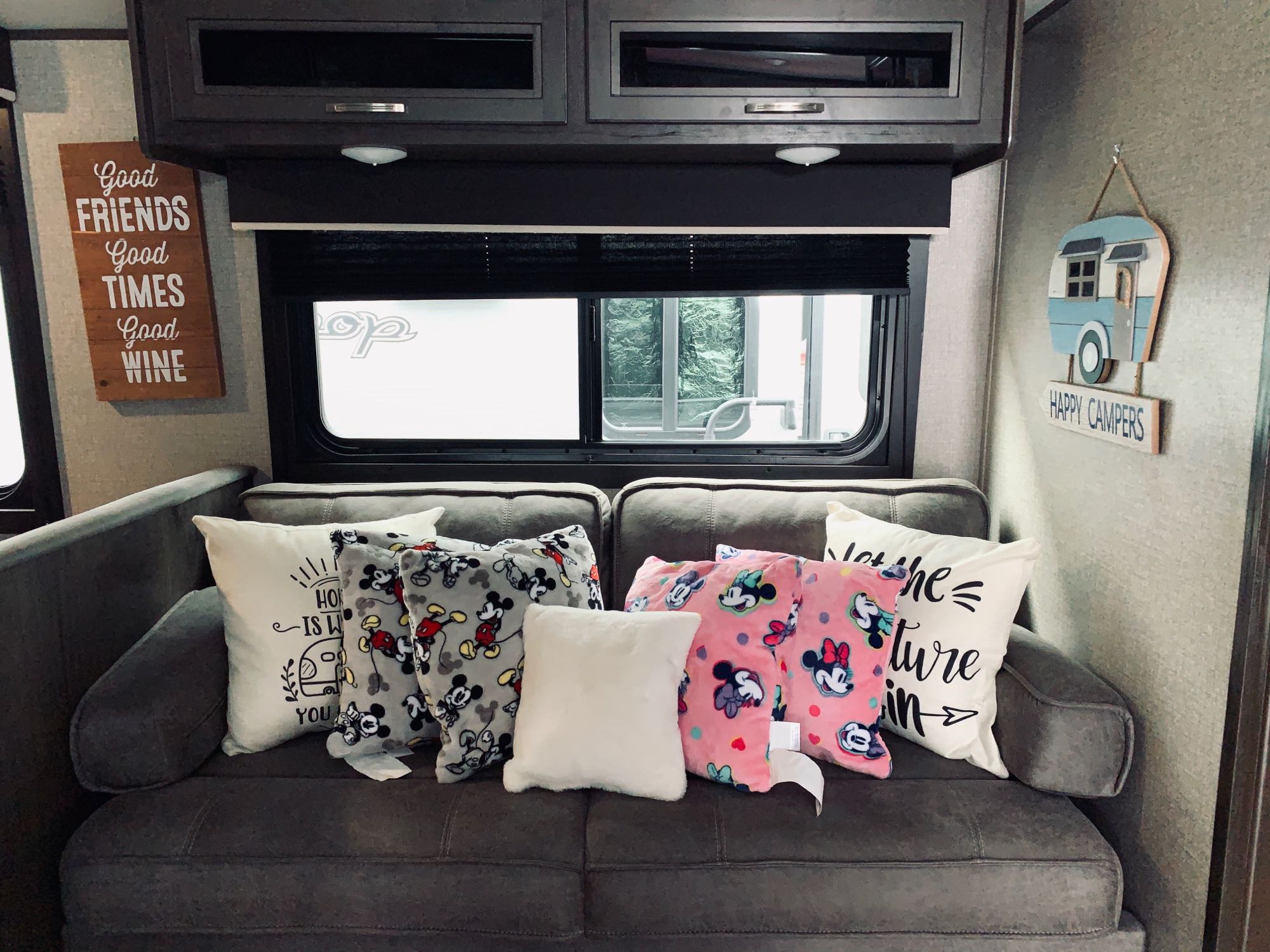 Step into this inviting RV rental: a sofa with Disney pillows, an 'adventure' sign, and 'Happy Campers' decor creating a cozy travel space.. Jayco Other 2021