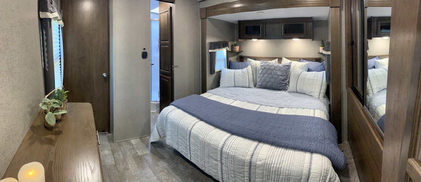 Step into this comfortable RV rental bedroom, featuring a large bed, modern decor, and a convenient private bathroom.. Forest River Rockwood Signature 2021