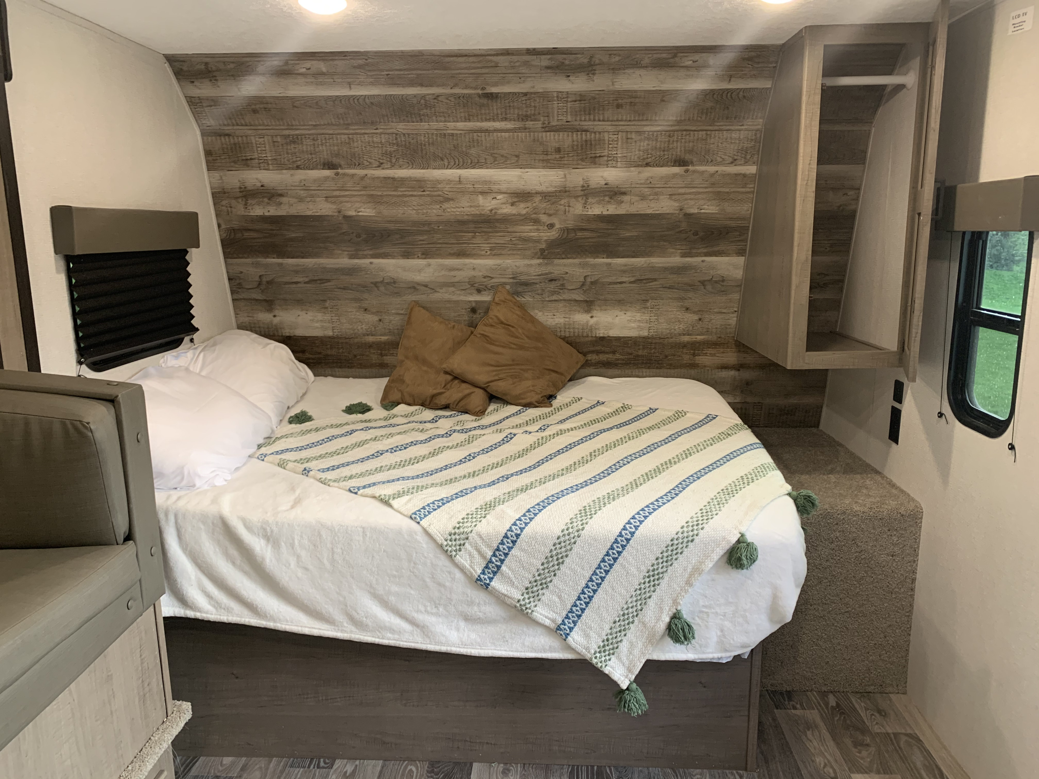Inside your RV rental: a compact and cozy bedroom with a comfortable bed, rustic wood walls, and clever storage solutions.. Keystone Hideout 2021
