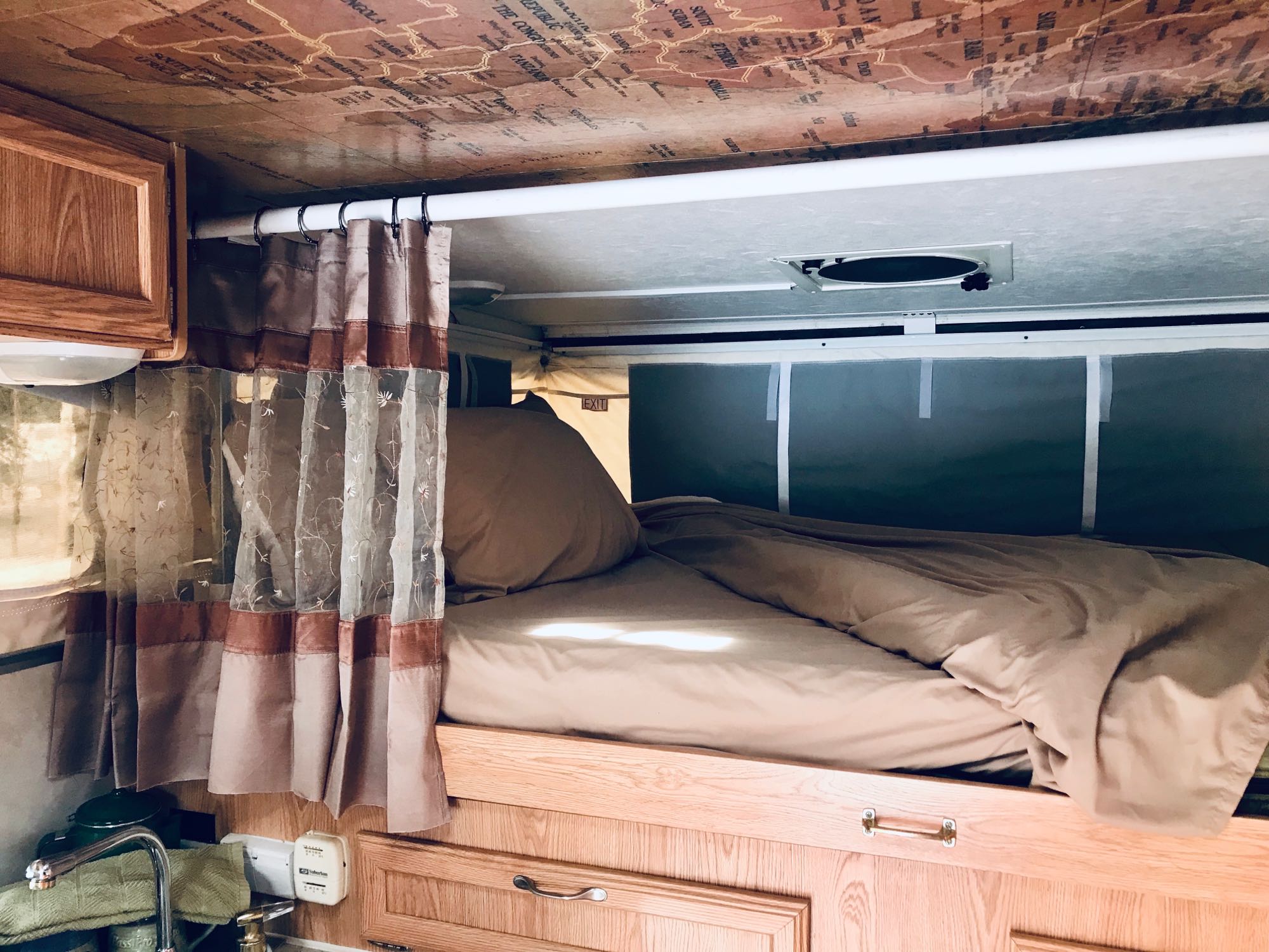 Cozy RV rental interior with a comfy bed, functional sink area, and unique map-patterned ceiling.. Ford F250 2005