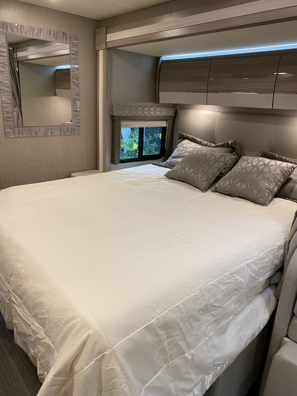 Experience comfort in this modern RV rental bedroom. Features include a spacious bed, overhead storage, and a stylish mirror.. Thor Delano 2021