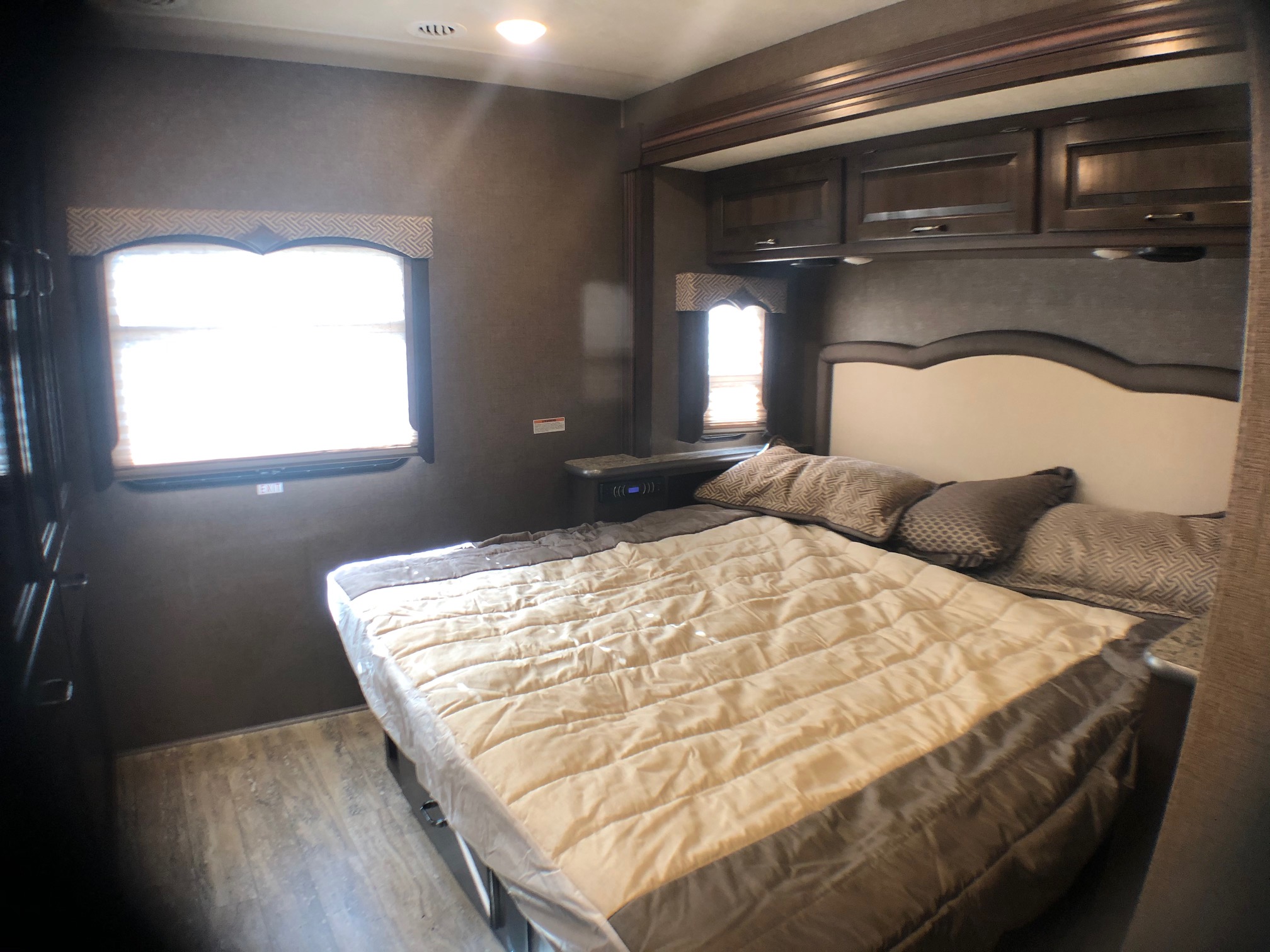 Cozy RV rental bedroom interior with a large bed, overhead cabinets, and bright windows on the wall.. THOR HURRICANE 2019