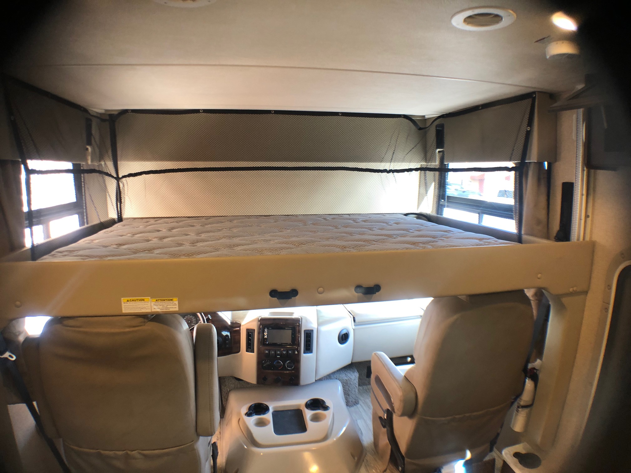 Spacious RV rental interior with an over-cab bunk bed, safety netting, and full view of the driver's cockpit.. THOR HURRICANE 2019
