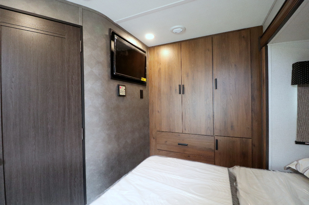 This RV rental bedroom offers practical living with a wall-mounted TV, ample wood-toned storage, and a comfy bed.. Forest River Forester 2021