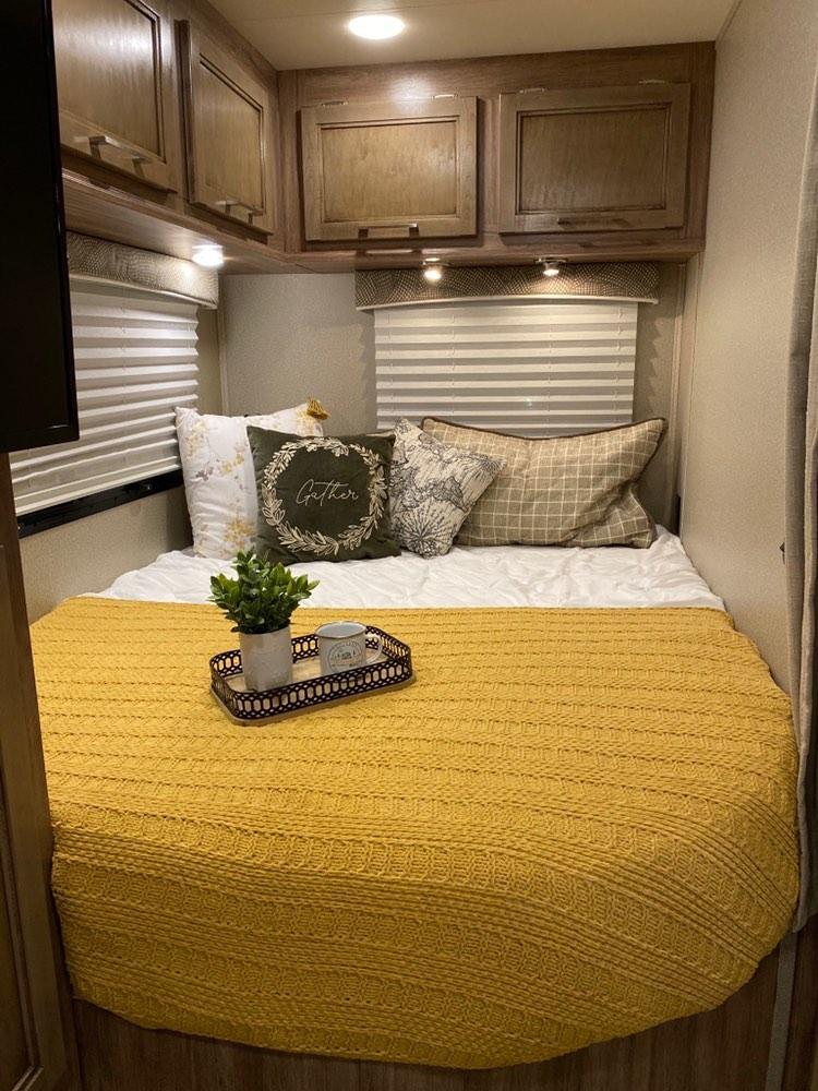 A beautifully decorated RV rental bedroom, featuring a vibrant yellow blanket, decorative pillows, and wood cabinetry.. Entegra Coach Odyssey 2019